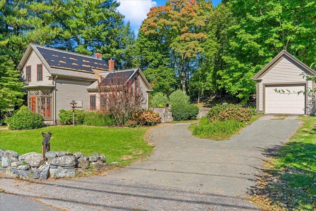 Two-story house and detached garage beside a broad driveway, lawn, and mature trees.