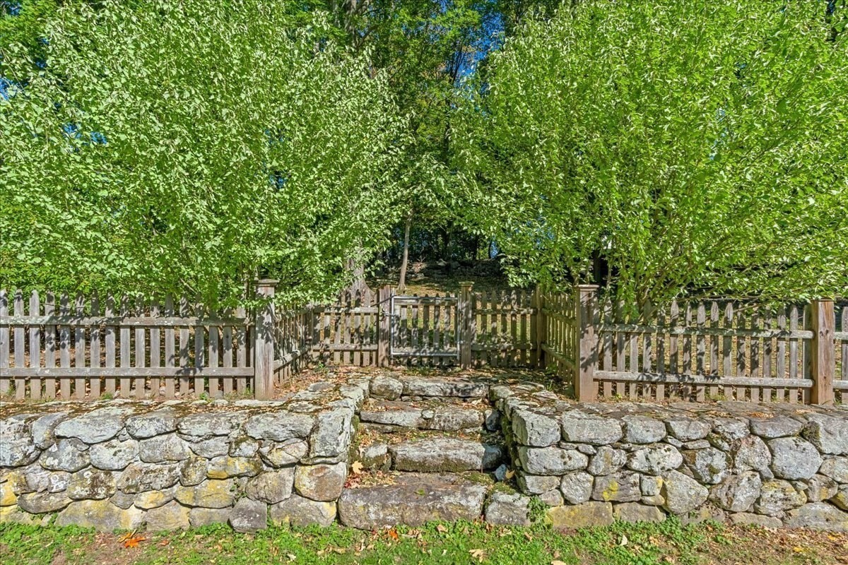 Stone steps lead through a low retaining wall to a wooden gate beneath leafy trees.