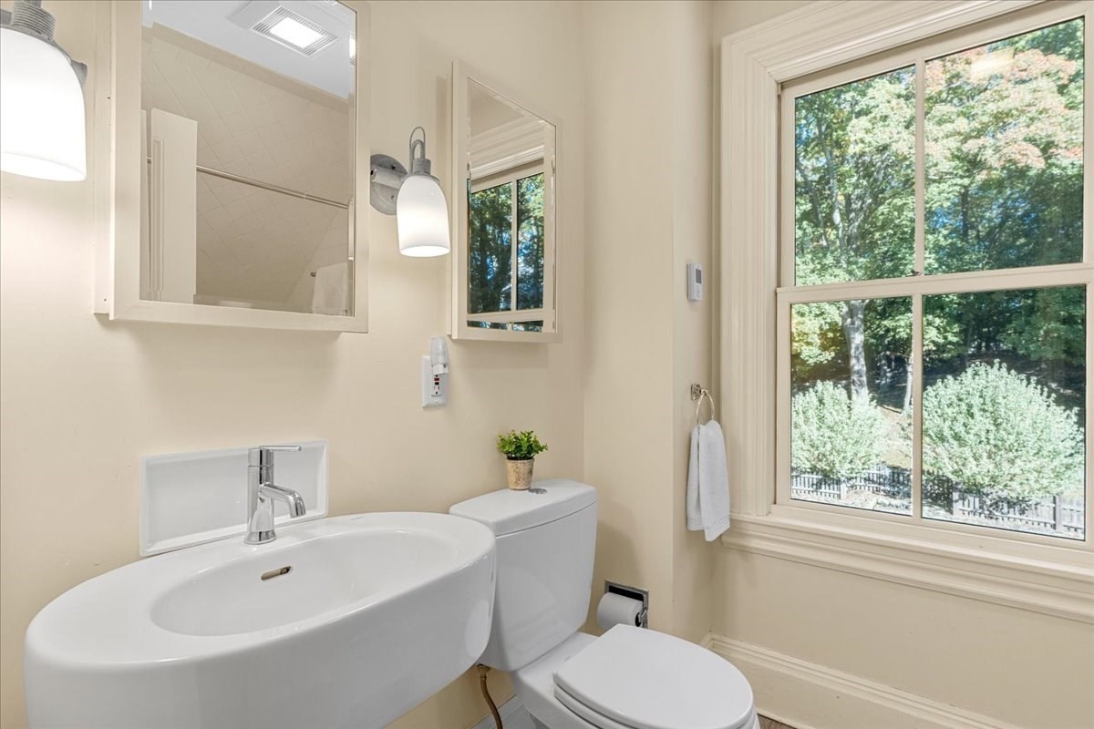 Bathroom with a wall-mounted sink and toilet beside a large window overlooking trees.
