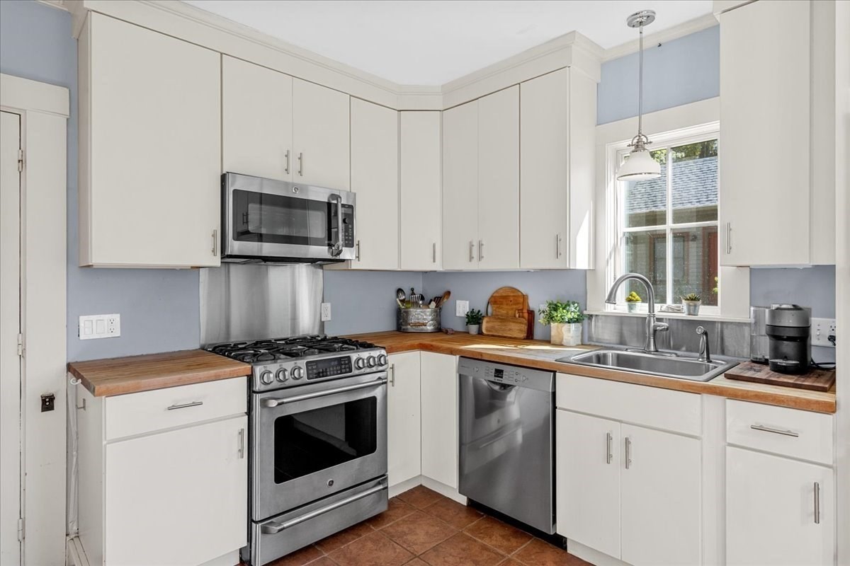 Kitchen with white cabinetry, wood countertops, and stainless steel appliances.