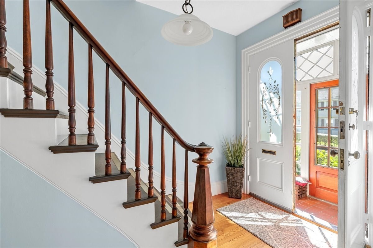 Entry foyer with a dark wood staircase, hardwood floor, and glass-paneled front door.