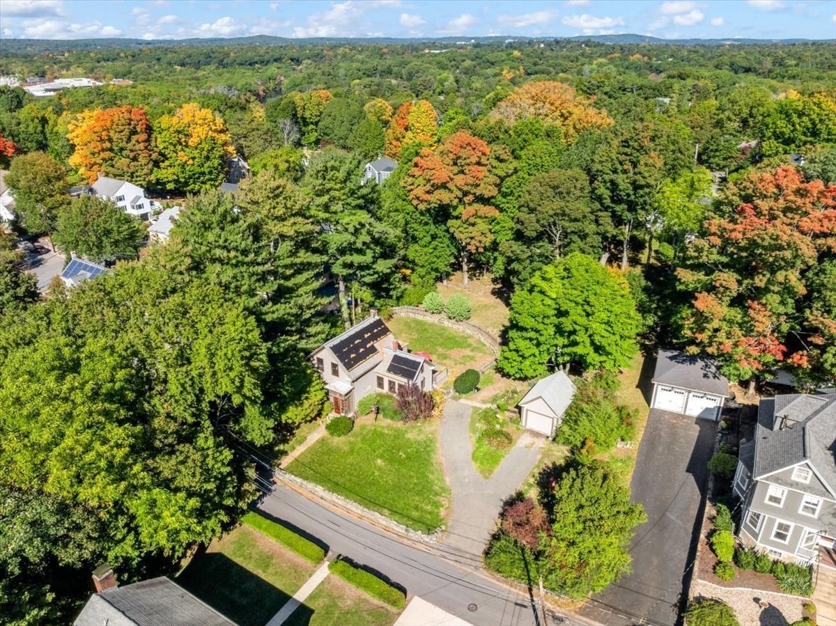 Aerial view of a house with rooftop solar panels and a curved driveway amid autumn trees.