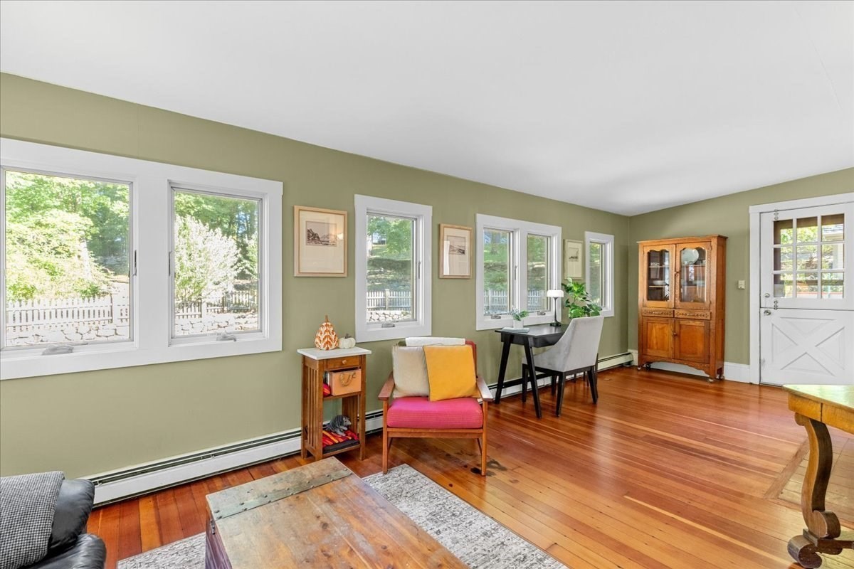Living and dining area with sage-green walls, hardwood floors, and multiple windows overlooking greenery.