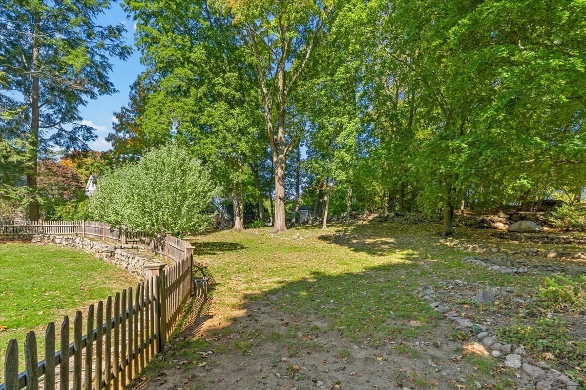 Tree-shaded backyard with a wooden picket fence and stone retaining wall.