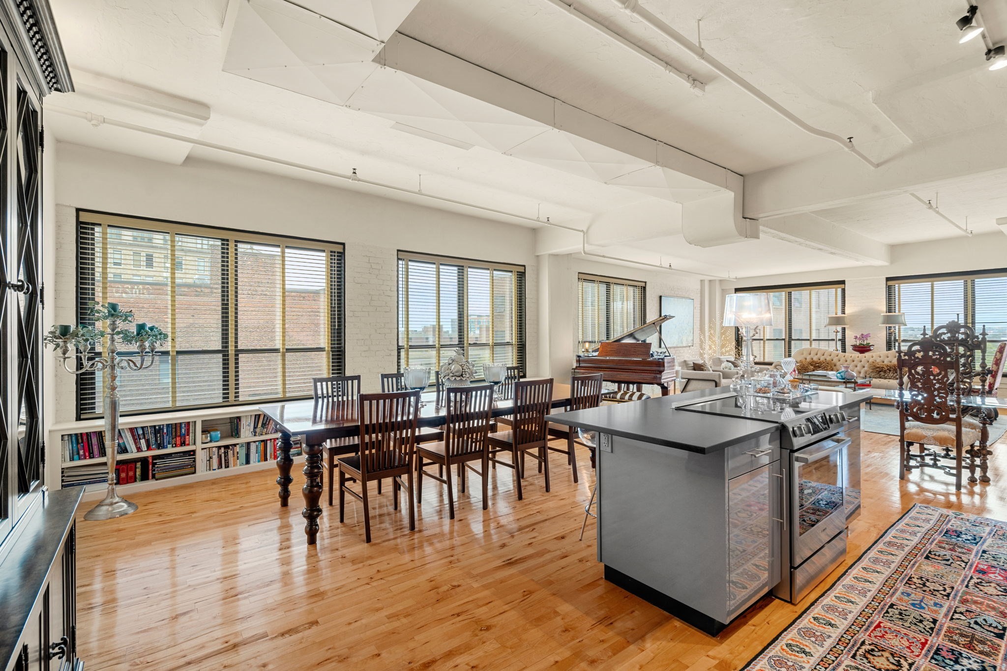Open-plan loft kitchen and dining area with hardwood floors, large windows, and a grand piano in the living area.