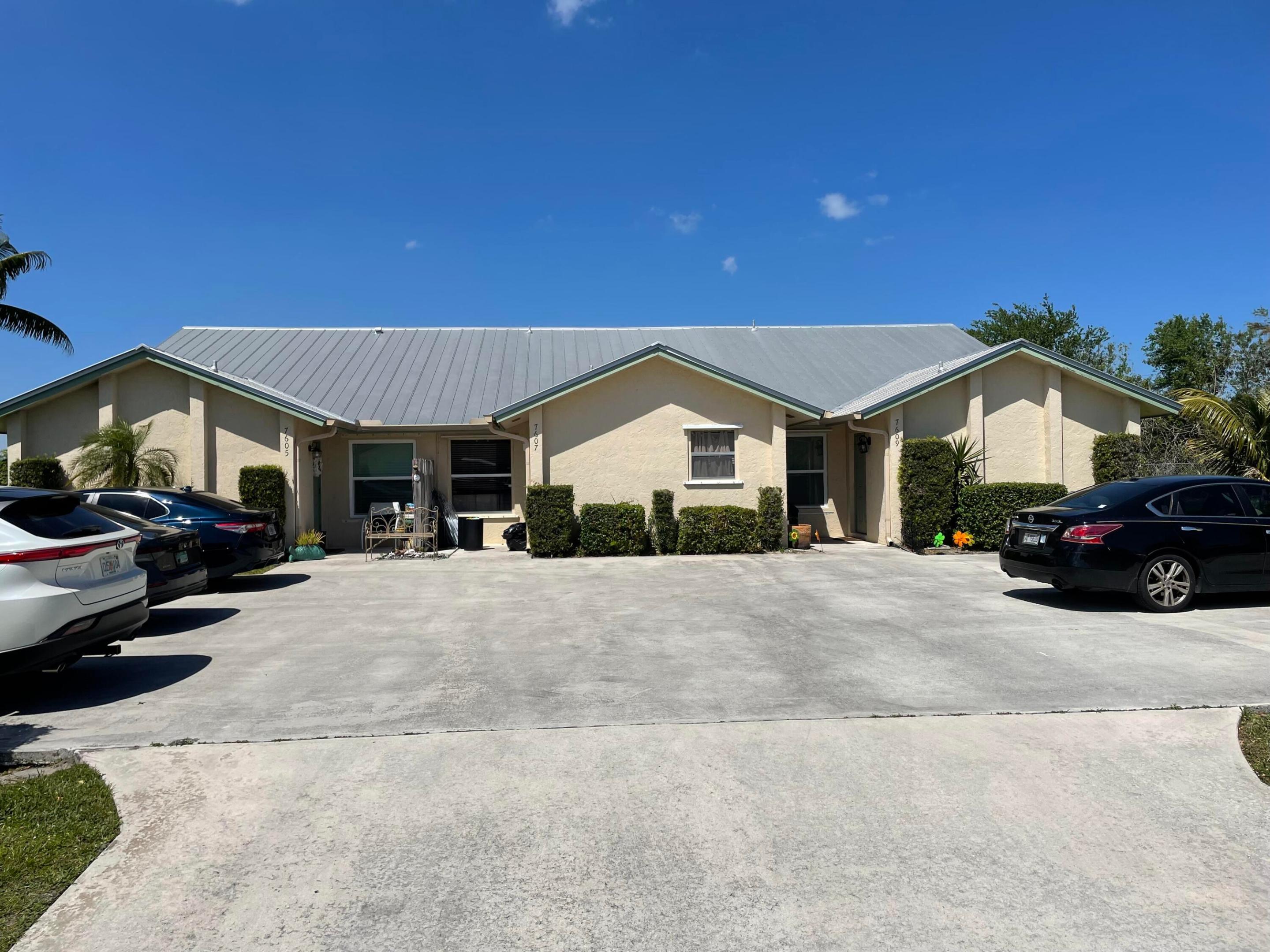 Cream stucco residential building with a metal roof and parked cars across the front.