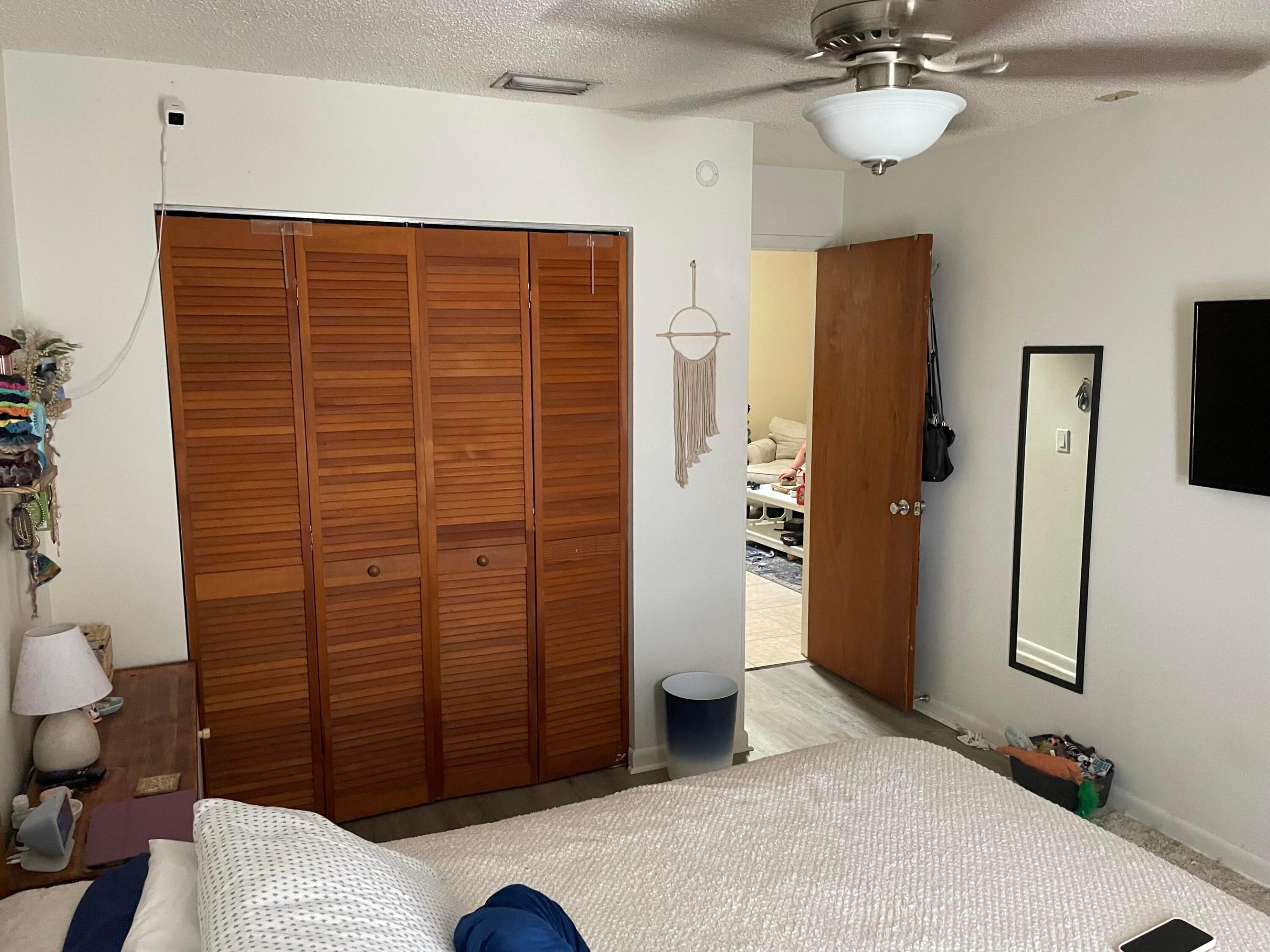 Bedroom with a bed, wooden louvered closet doors, and an open doorway to the adjoining room.