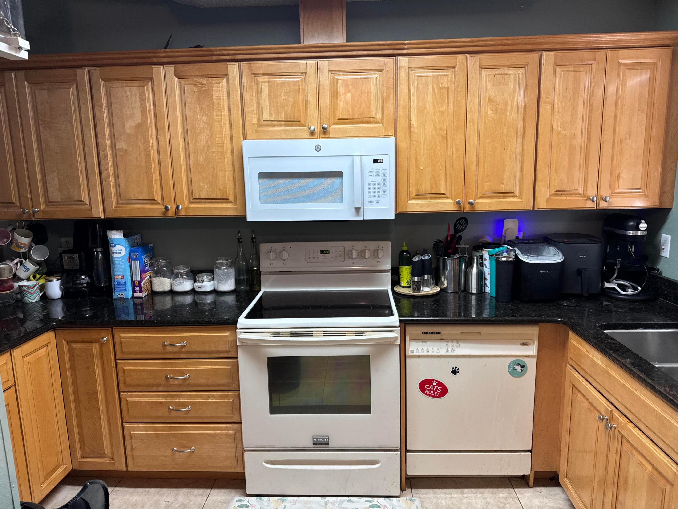 Kitchen with honey-colored cabinets, black counters, and white range and microwave.