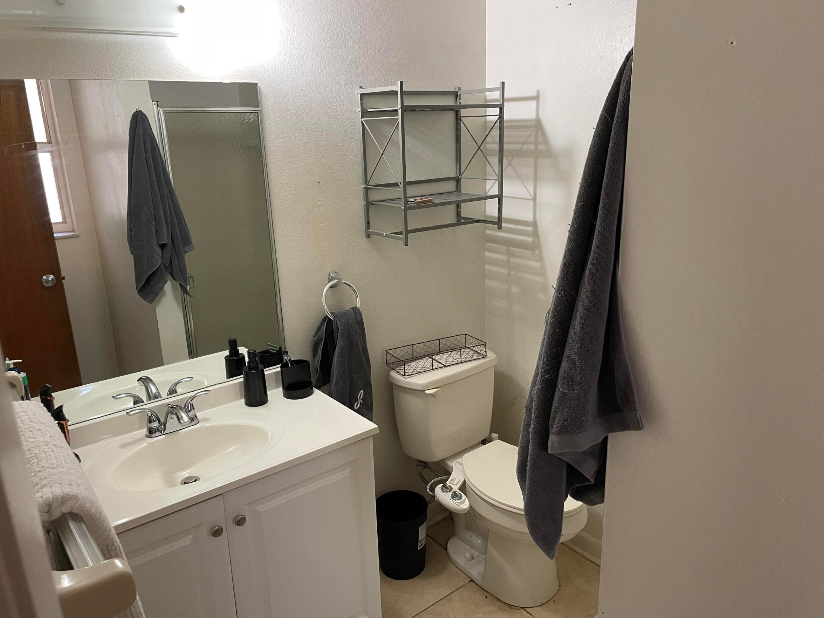 Bathroom with a white vanity and sink, toilet, wall shelving, and dark towels.