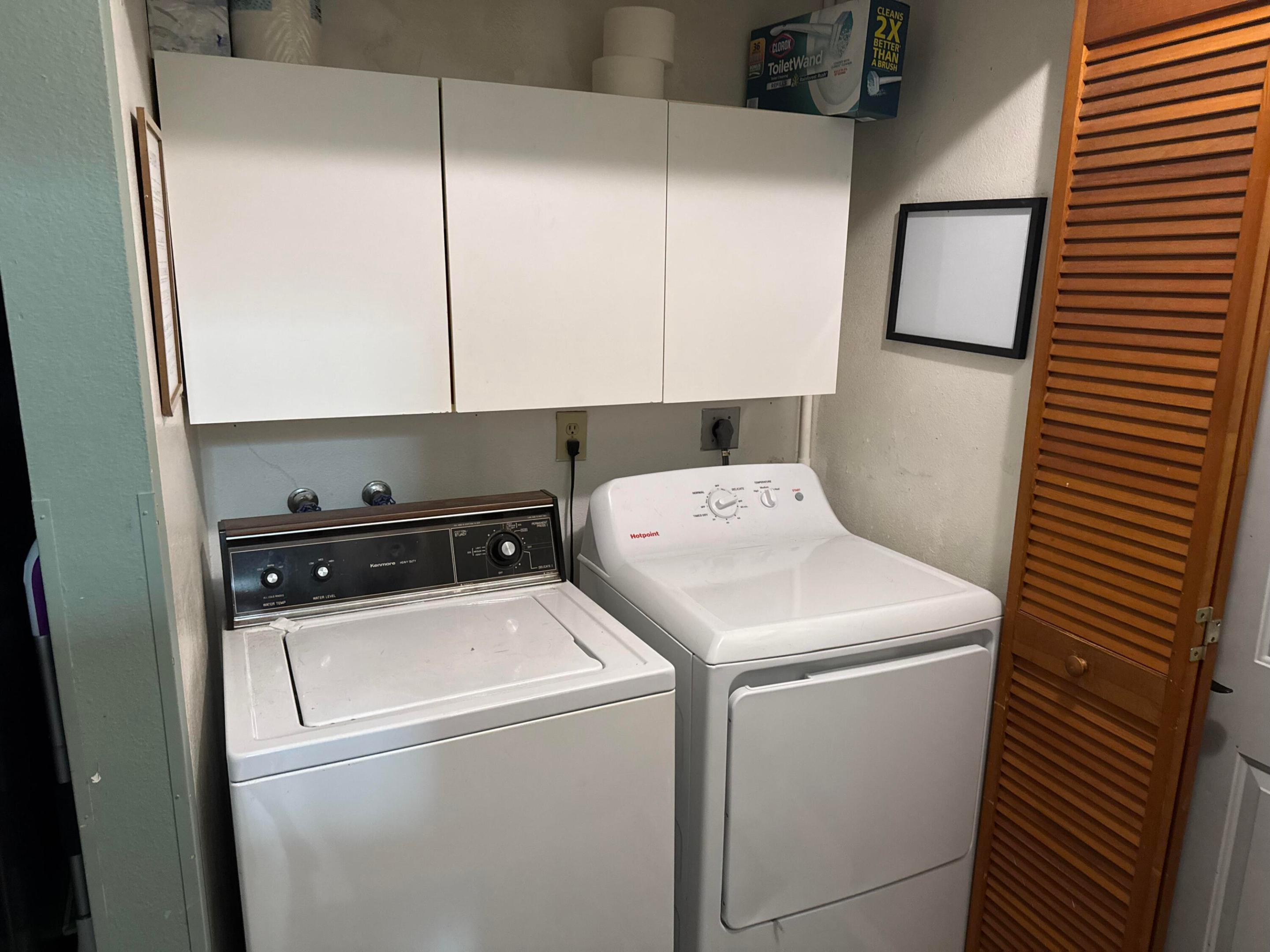Laundry room with a Kenmore washer, Hotpoint dryer, white cabinets, and a wooden louvered door.