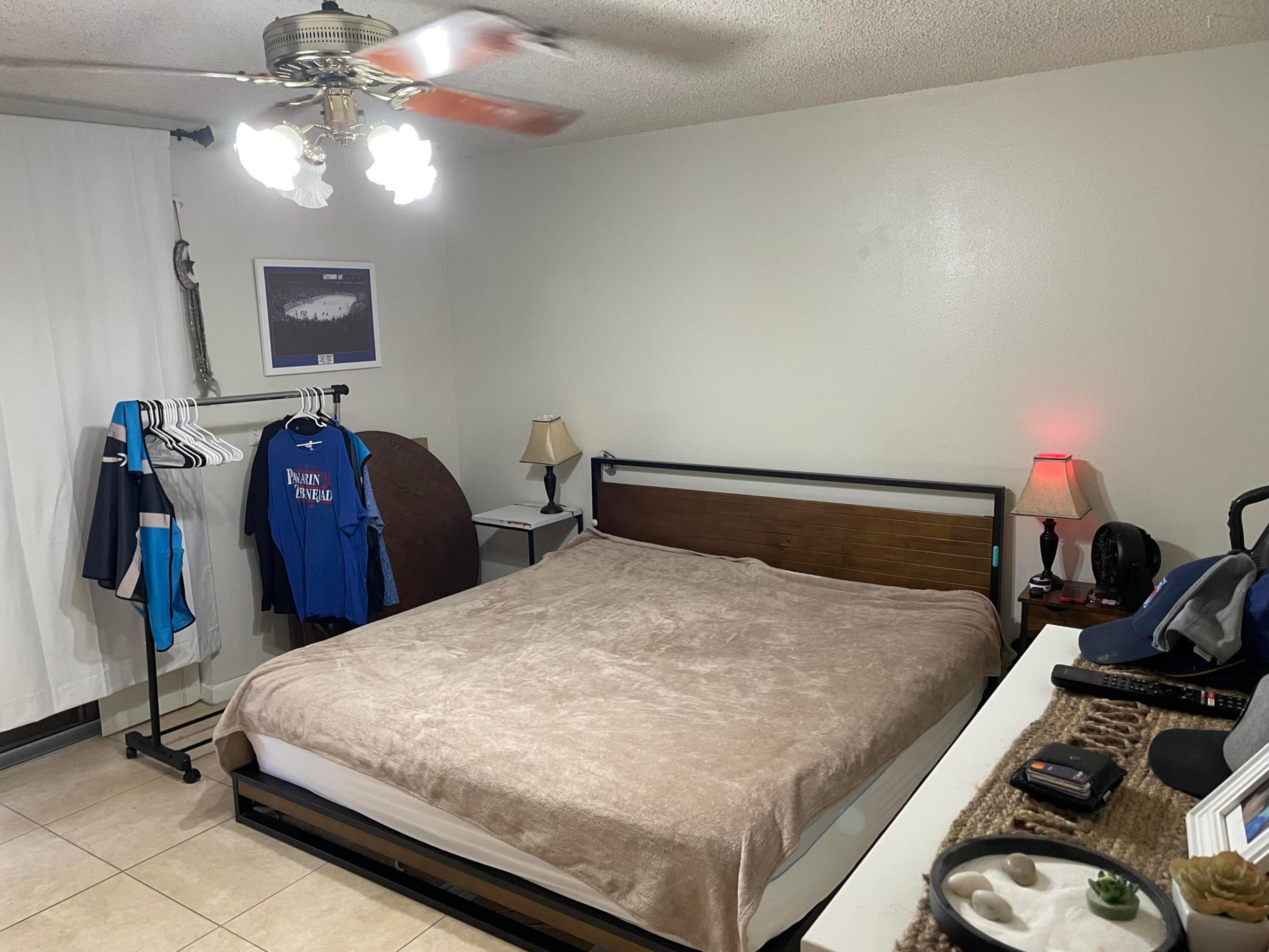 Bedroom with a large beige-covered bed, wood headboard, and clothing rack.