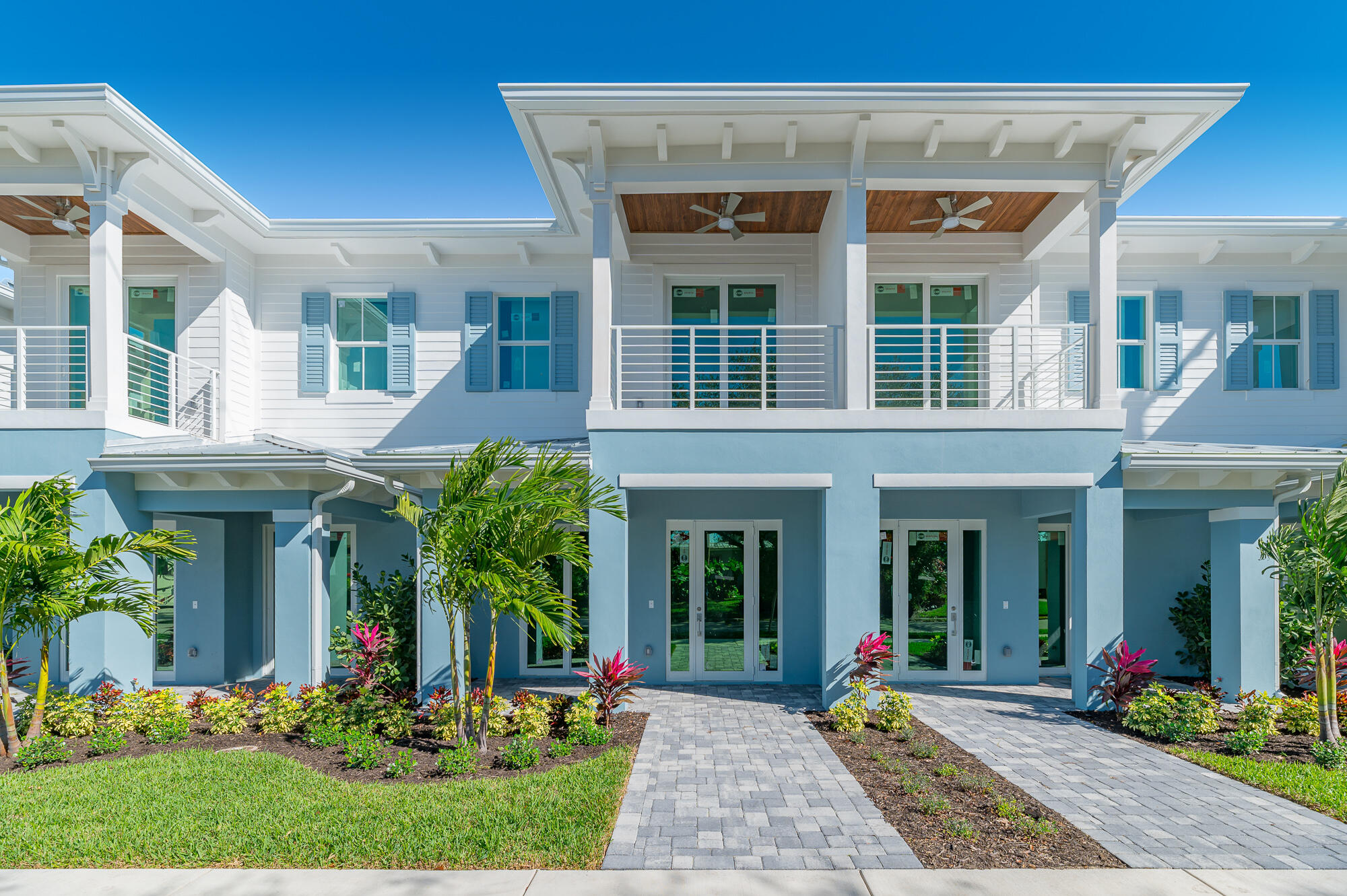 Light blue two-story home with a covered balcony, wood-paneled porch ceilings, and tropical landscaping.