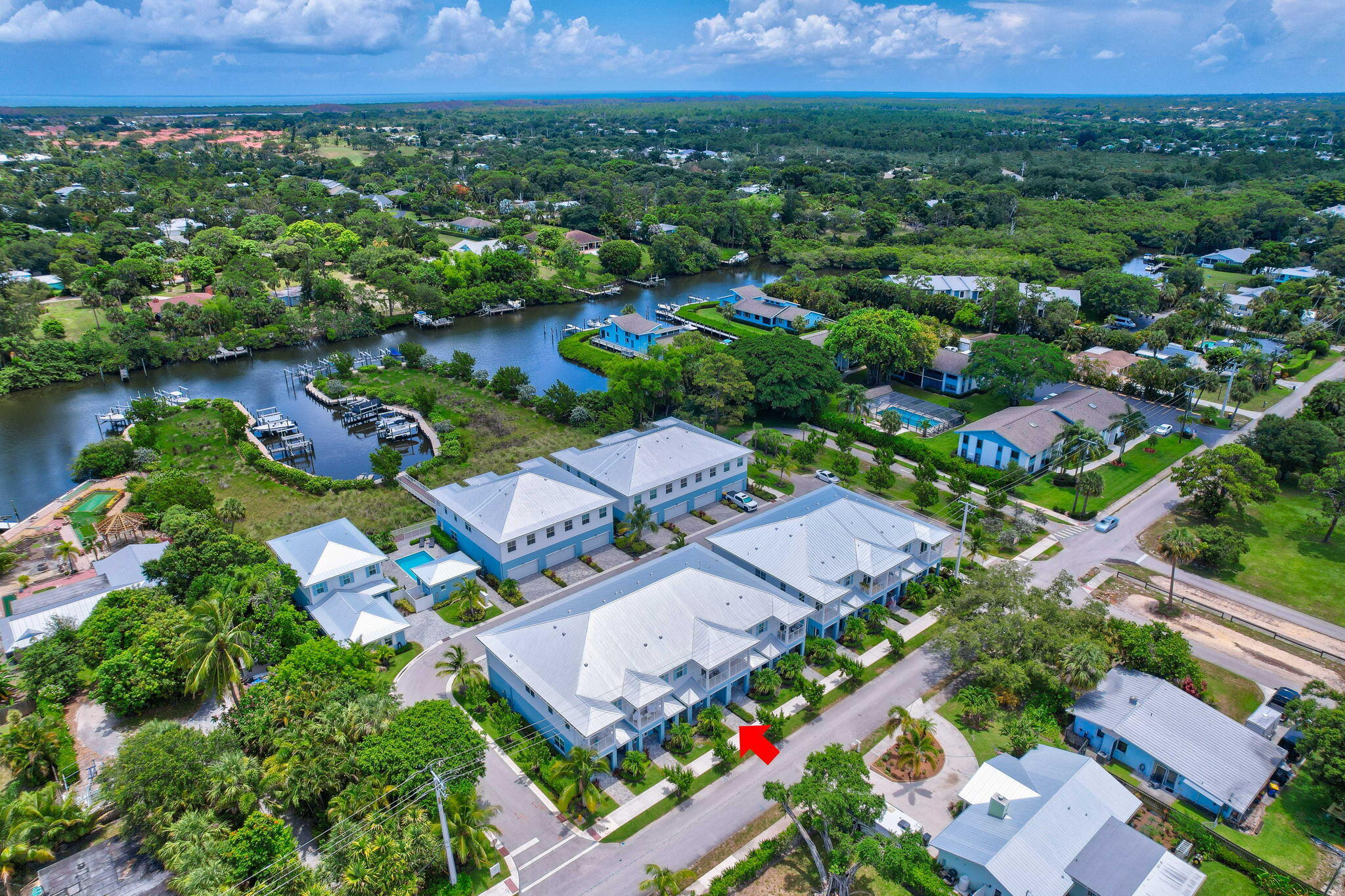 Aerial view of a blue-and-white residential building marked by a red arrow, beside a canal with docks.