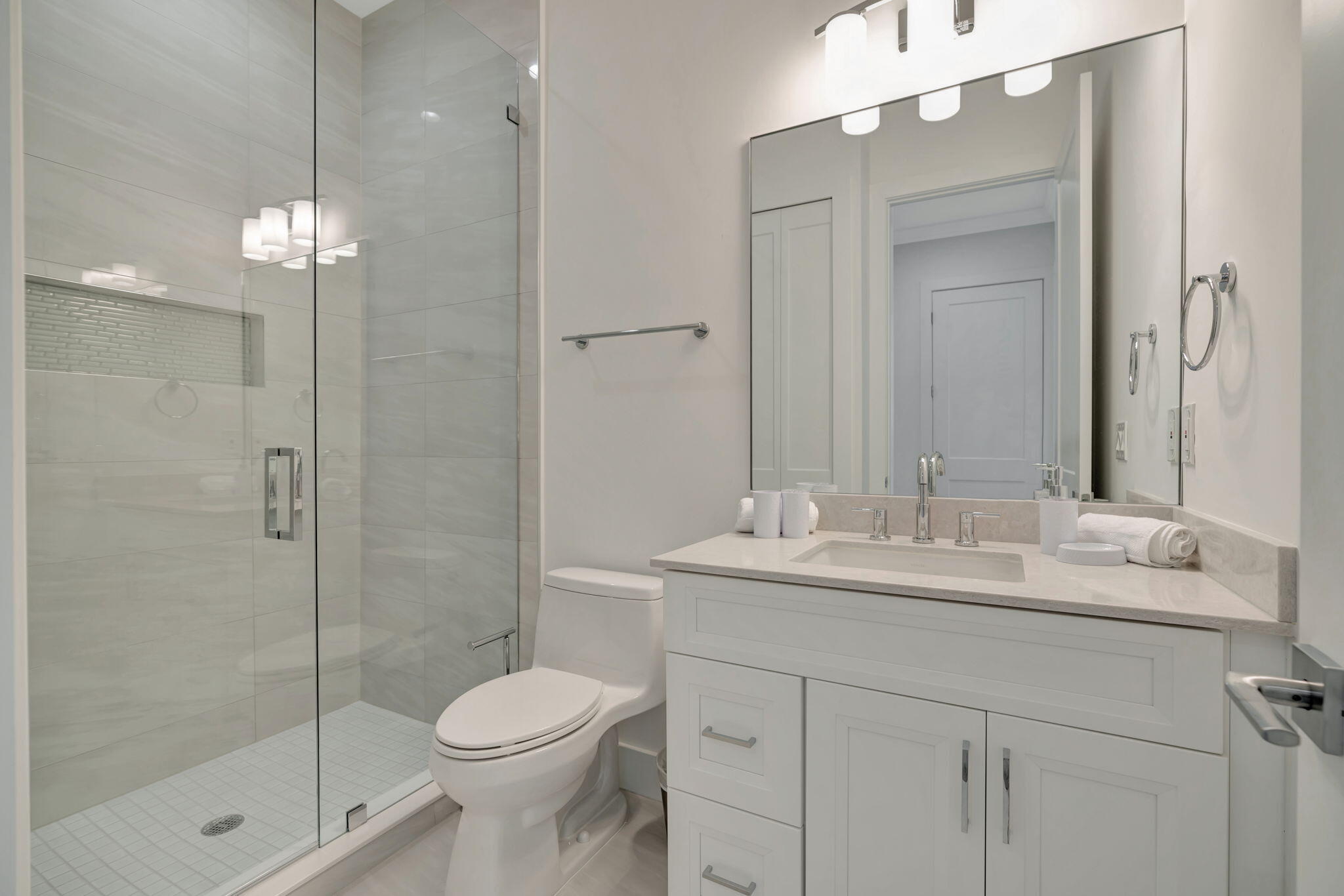 Modern bathroom with glass walk-in shower, white vanity, and large mirror.