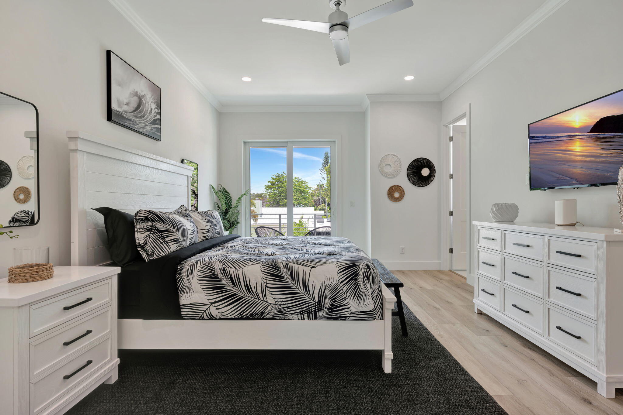 Bedroom with black-and-white leaf-patterned bedding, white furniture, and a sliding glass door to a balcony.