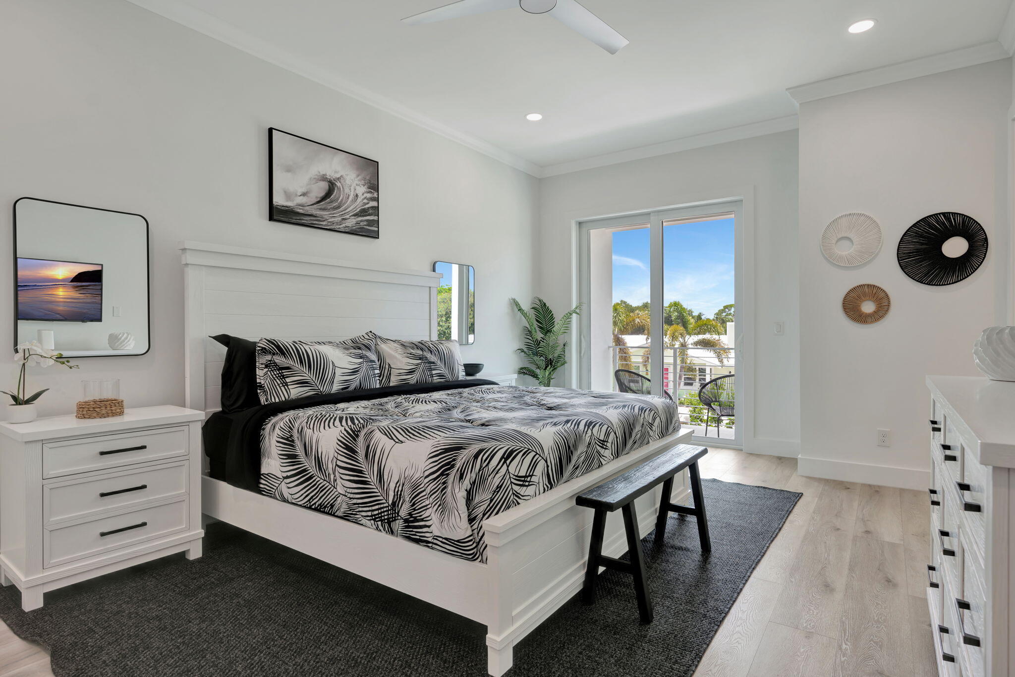 Staged bedroom with black-and-white leaf-patterned bedding and sliding doors to a palm-lined balcony.