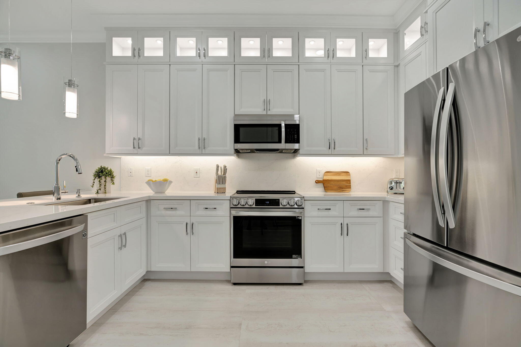 Modern kitchen with white cabinetry, pale stone counters, and stainless steel appliances.