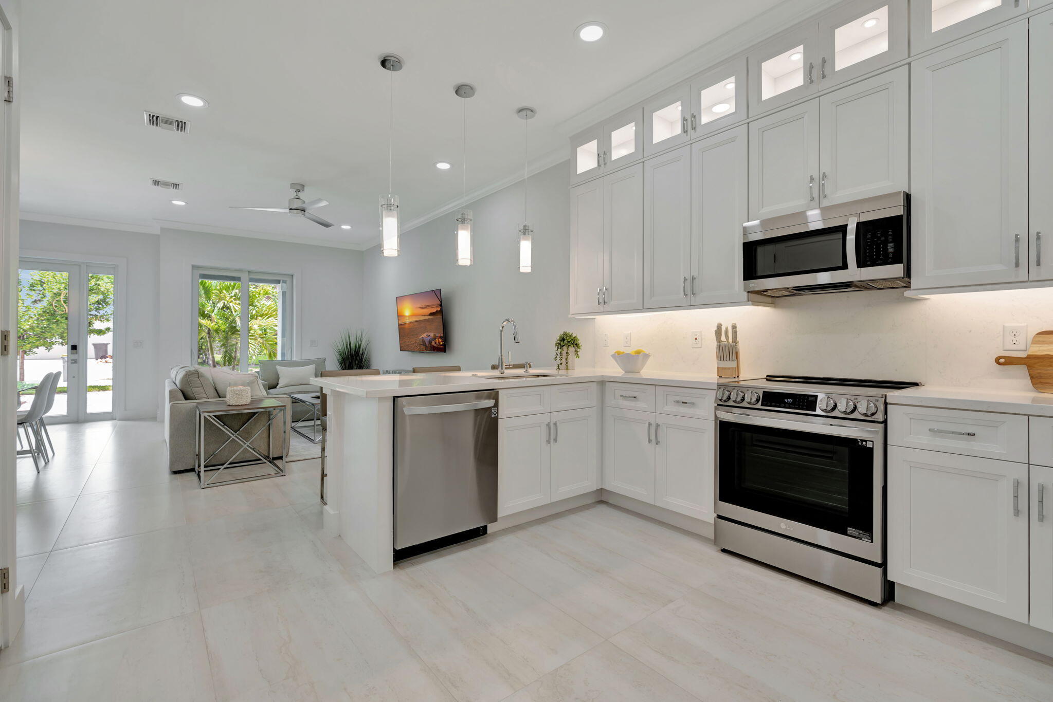 Open-plan kitchen with white cabinetry, a large island, and stainless steel appliances beside a furnished living area.