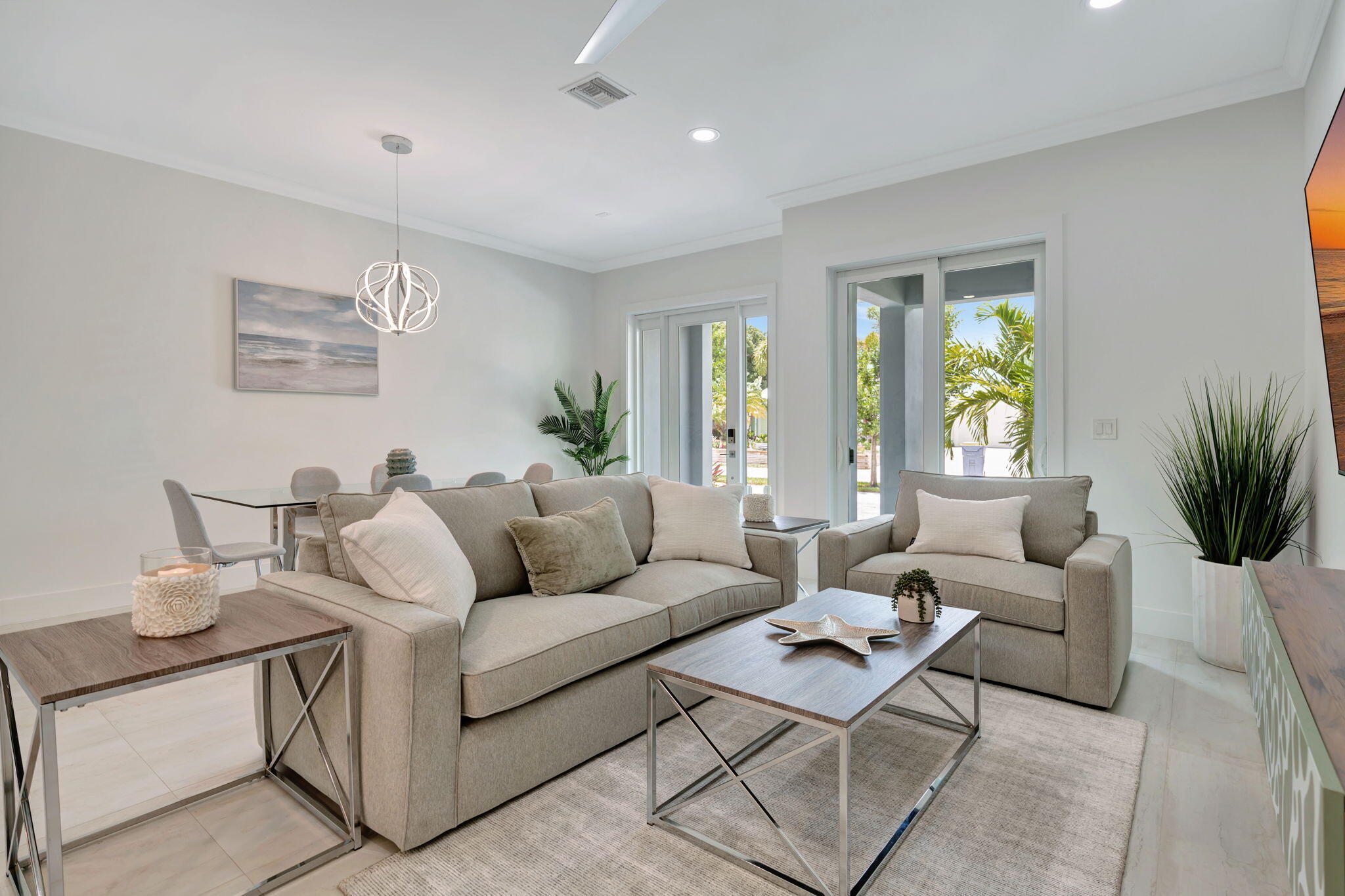 Staged living room with neutral sofas and sliding glass doors overlooking palm trees.