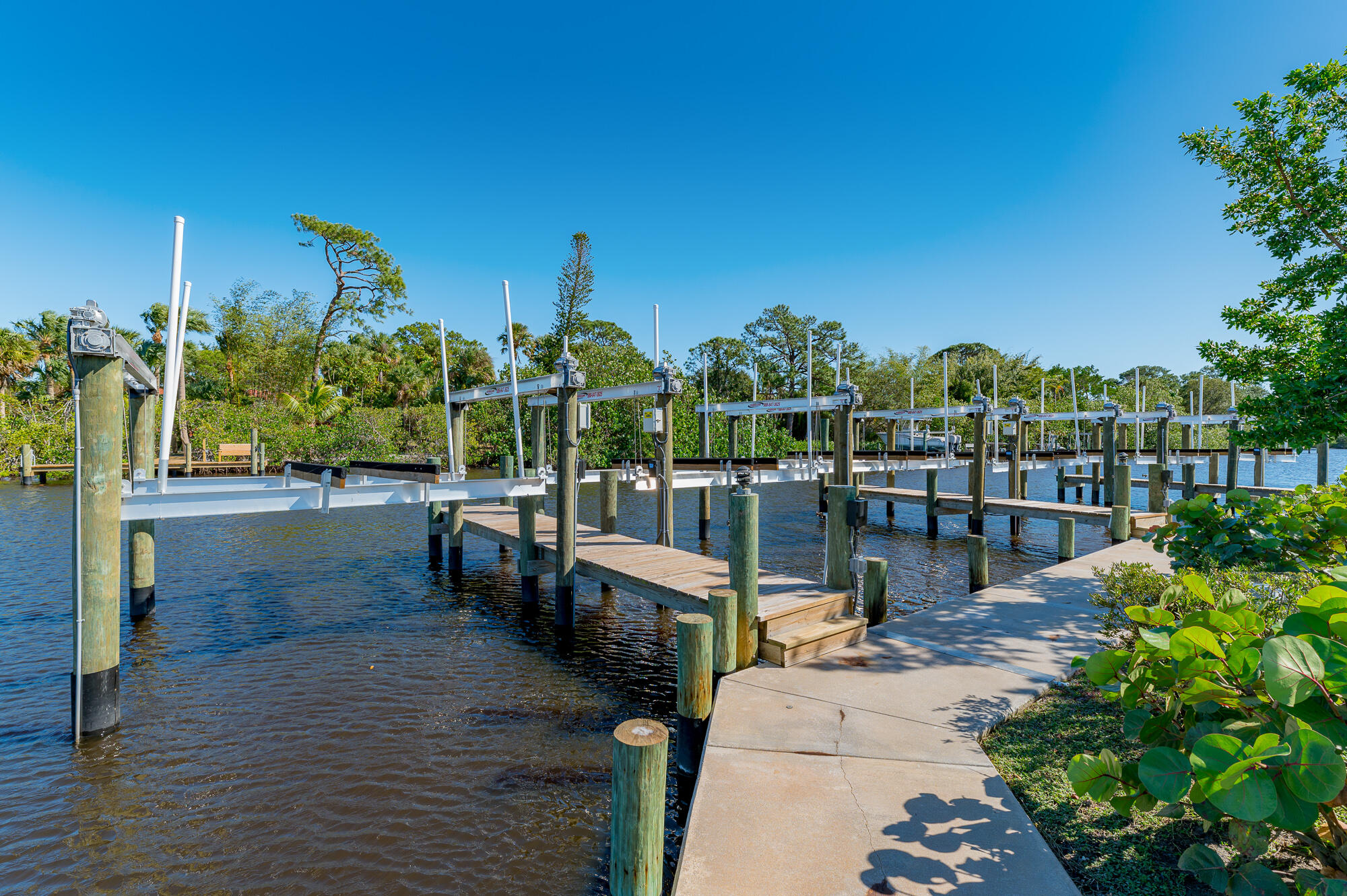 Waterfront docks with multiple boat lifts and a concrete walkway beside the water.