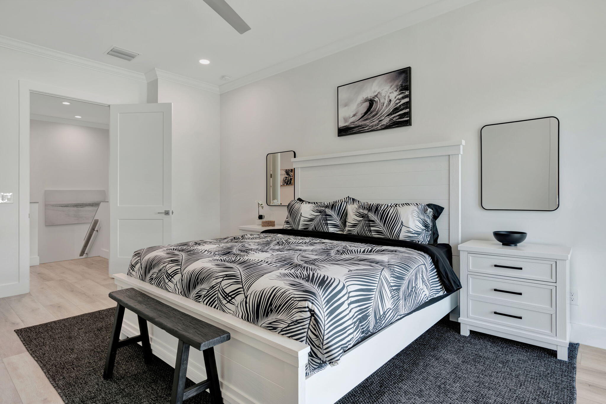 Furnished bedroom with a white bed, black-and-white leaf-patterned bedding, and a dark bench.