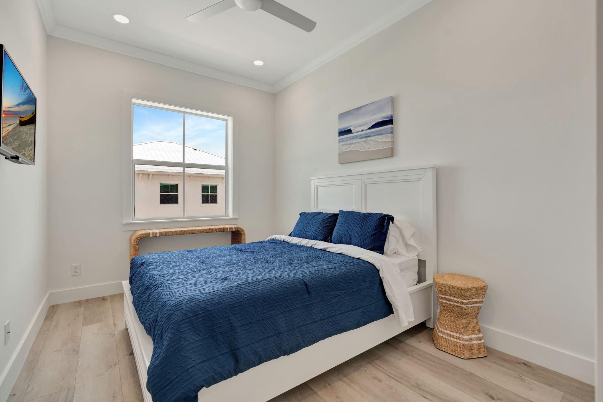 Bedroom with a white bed dressed in navy bedding beneath coastal artwork, beside a large window.