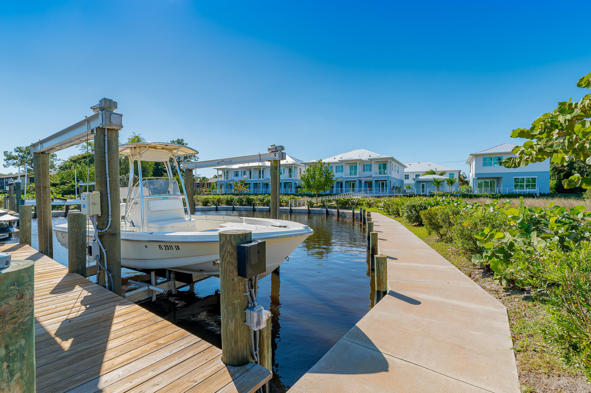 White boat at a wooden canal dock, with waterfront homes and a paved path nearby.