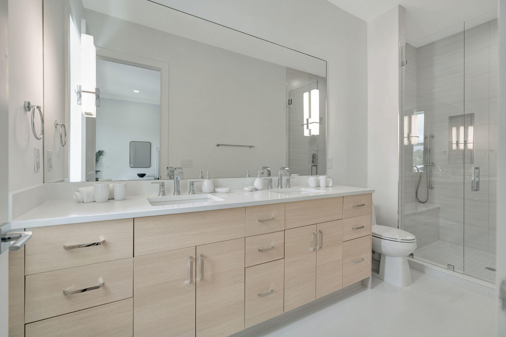 Modern bathroom with a light-wood double vanity, mirrored wall, and glass-enclosed shower.