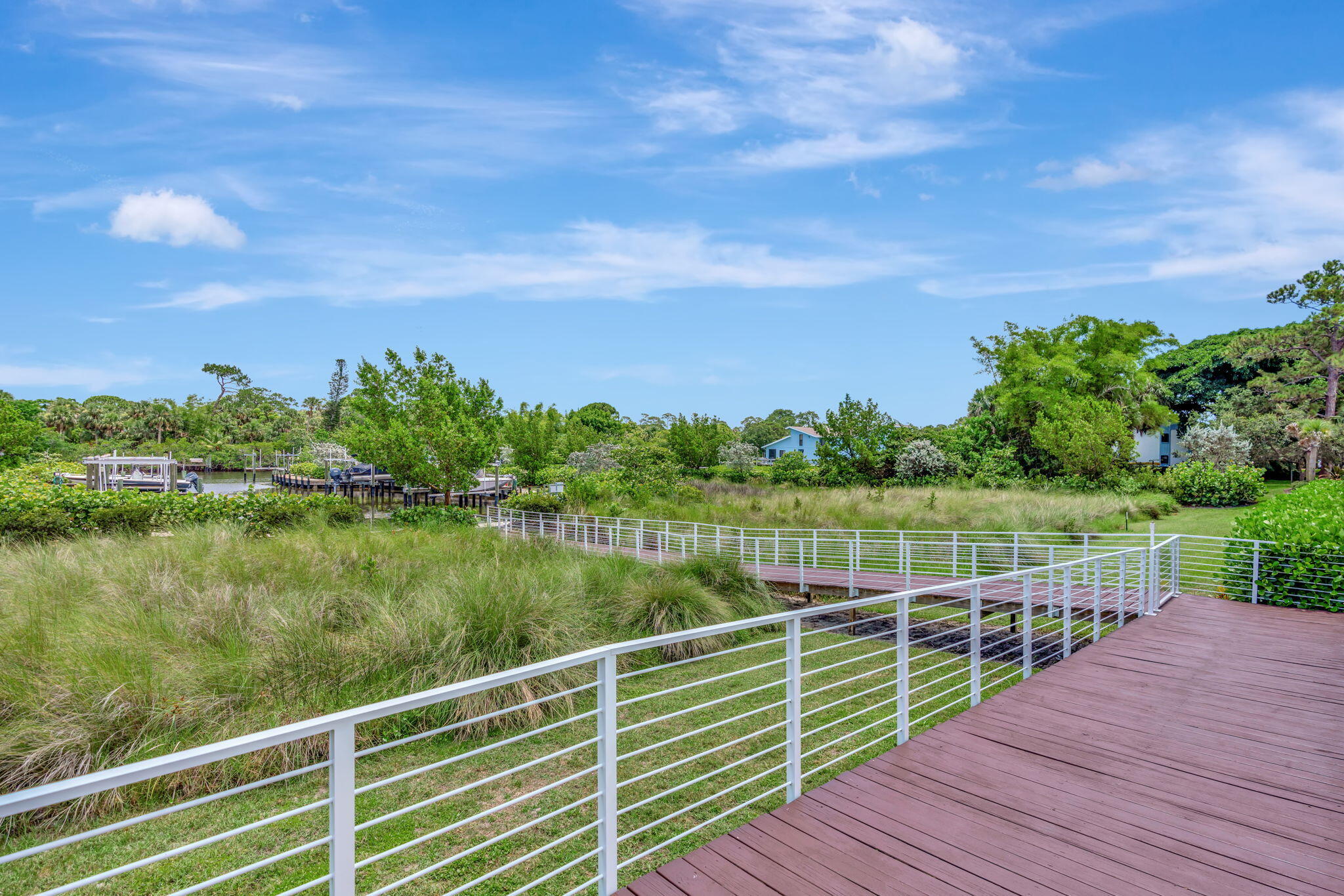 Waterfront boardwalk with white railings crossing coastal grasses toward a canal and neighboring docks.