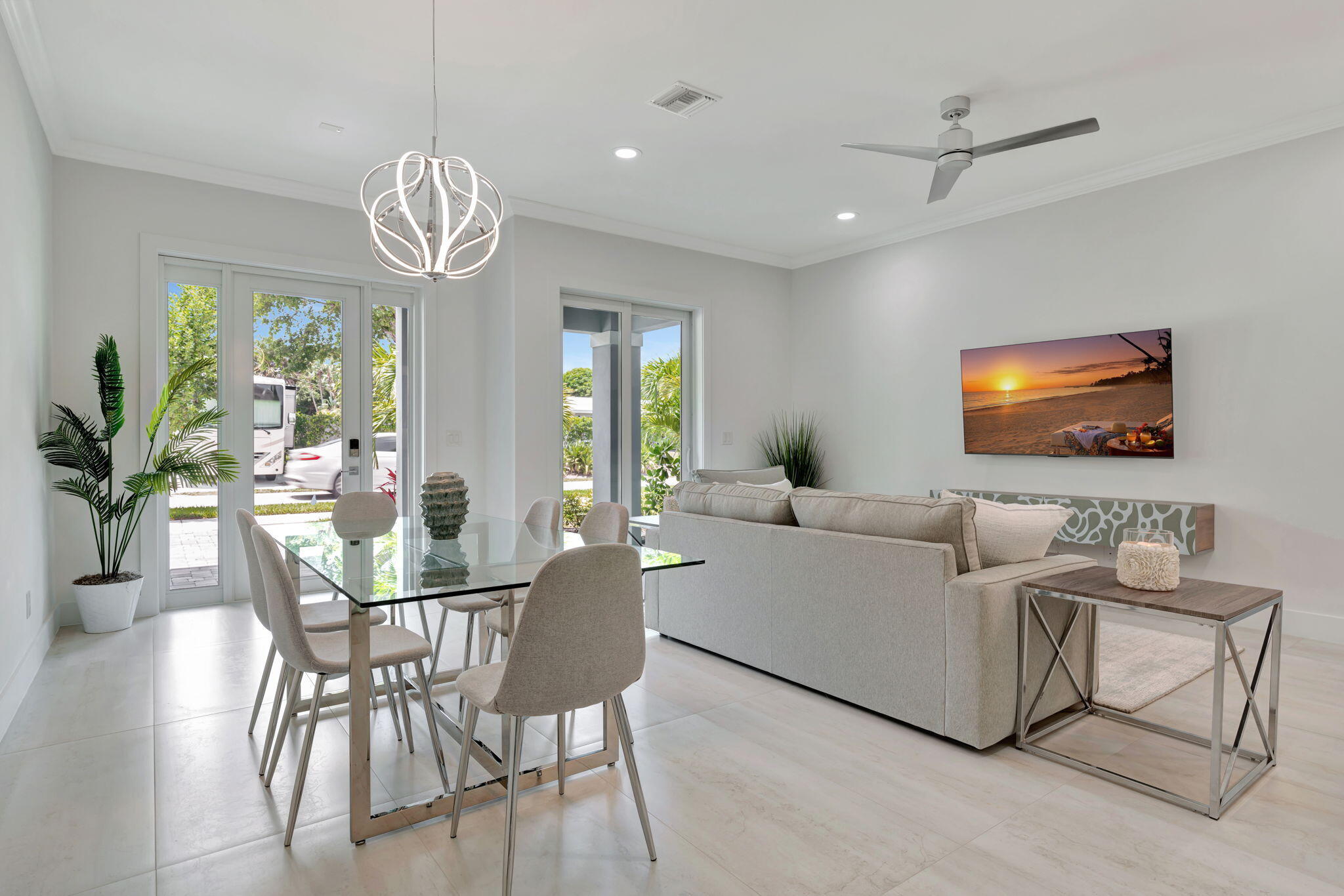 Open-plan living and dining room with a glass dining table, pale sectional, and large garden-facing glass doors.