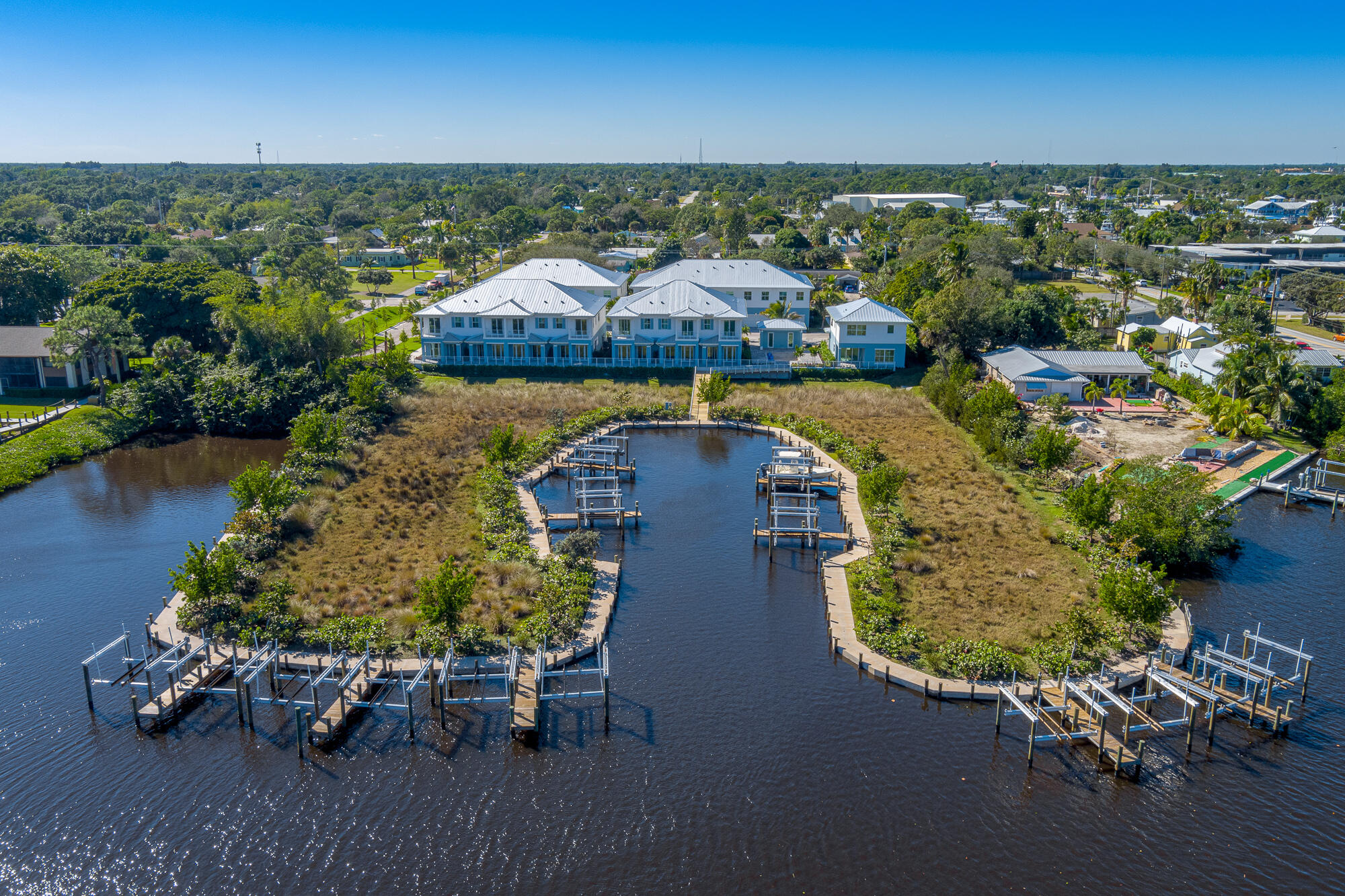 Waterfront homes and boat docks line a winding inlet beside a marshy shoreline.