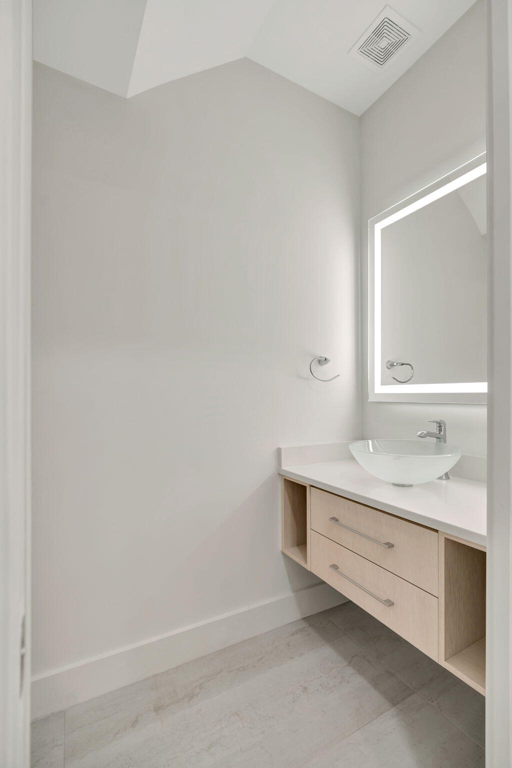 Bathroom with a floating light-wood vanity, vessel sink, and illuminated mirror.