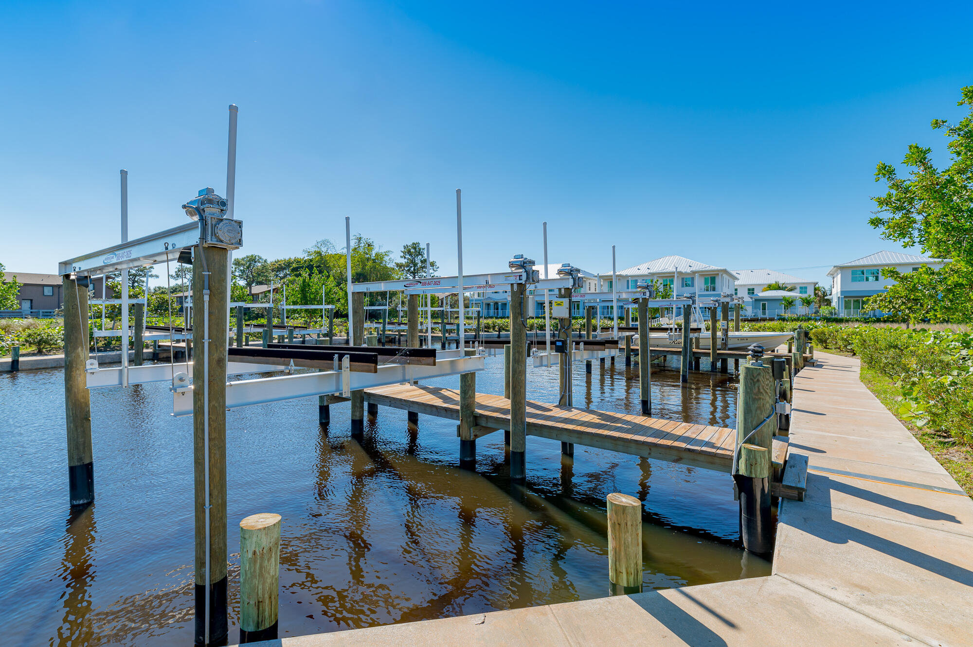 Waterfront marina with boat lifts, wooden docks, and homes across the canal.