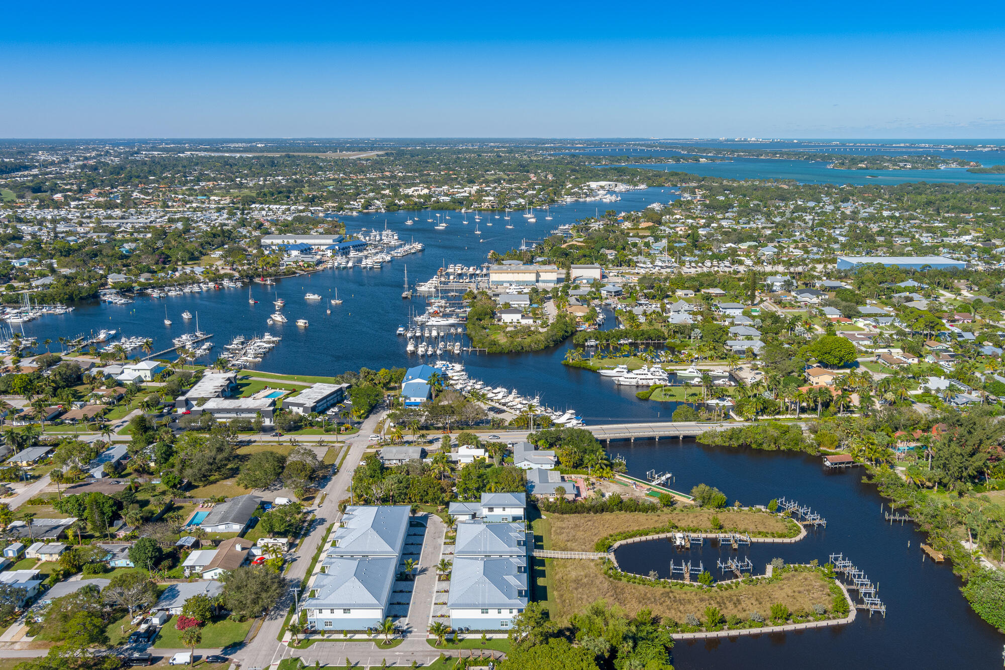 Aerial view of waterfront homes beside a marina, with boats, waterways, and a bridge.