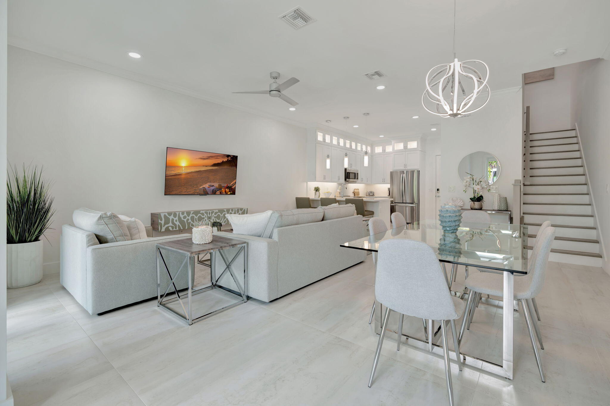 Open-plan living and dining room with pale sofas, a glass table, and a white kitchen.