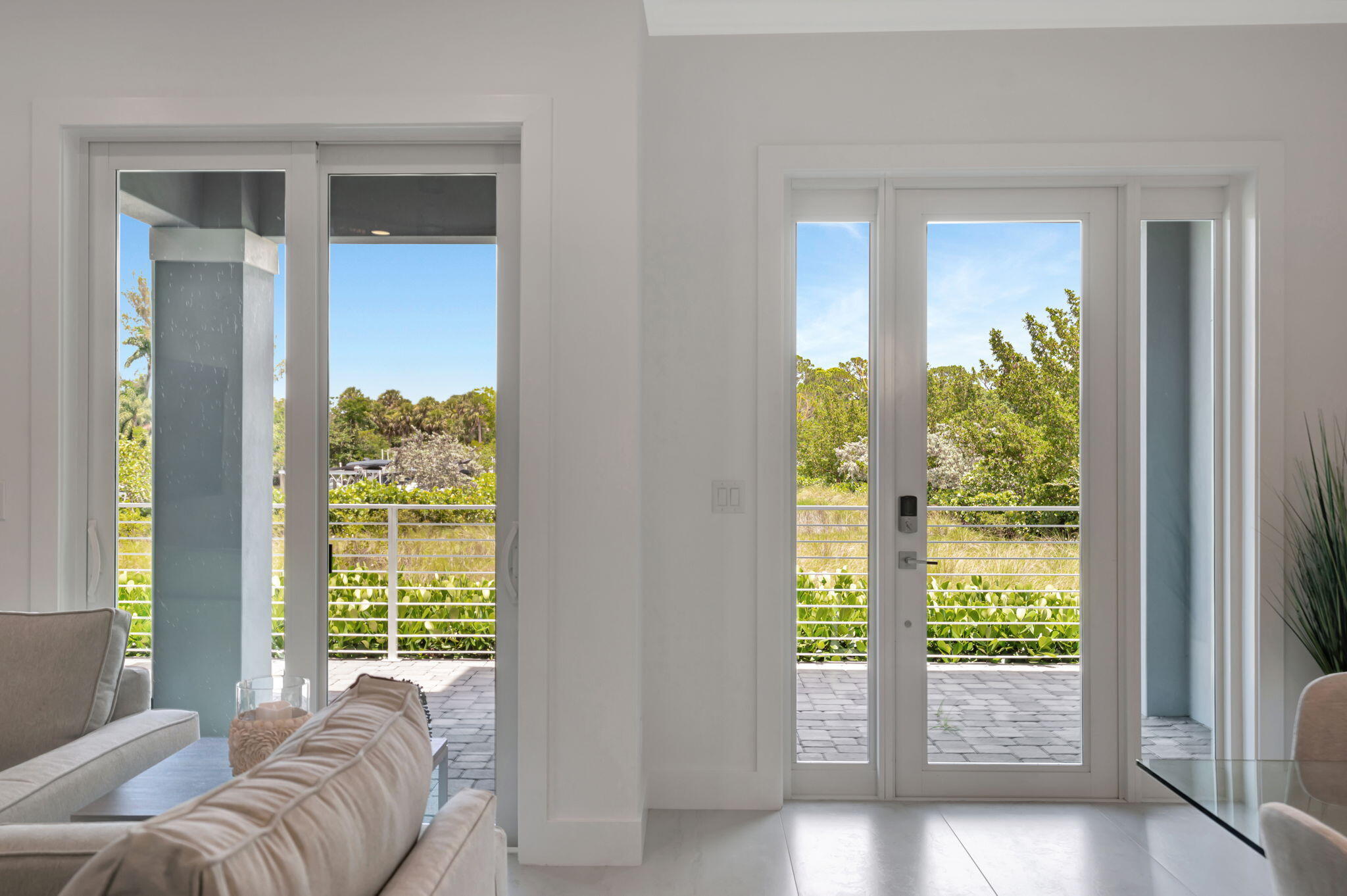 Living room with glass doors opening onto a paved patio and leafy greenery.