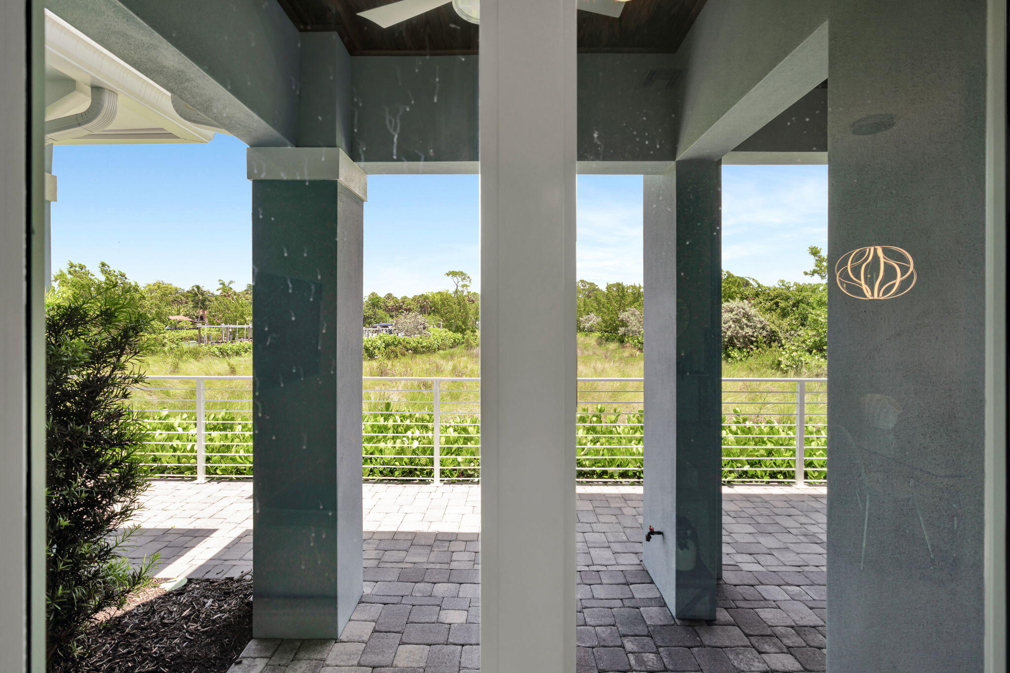 Covered patio with stone columns and pavers overlooking lush greenery.