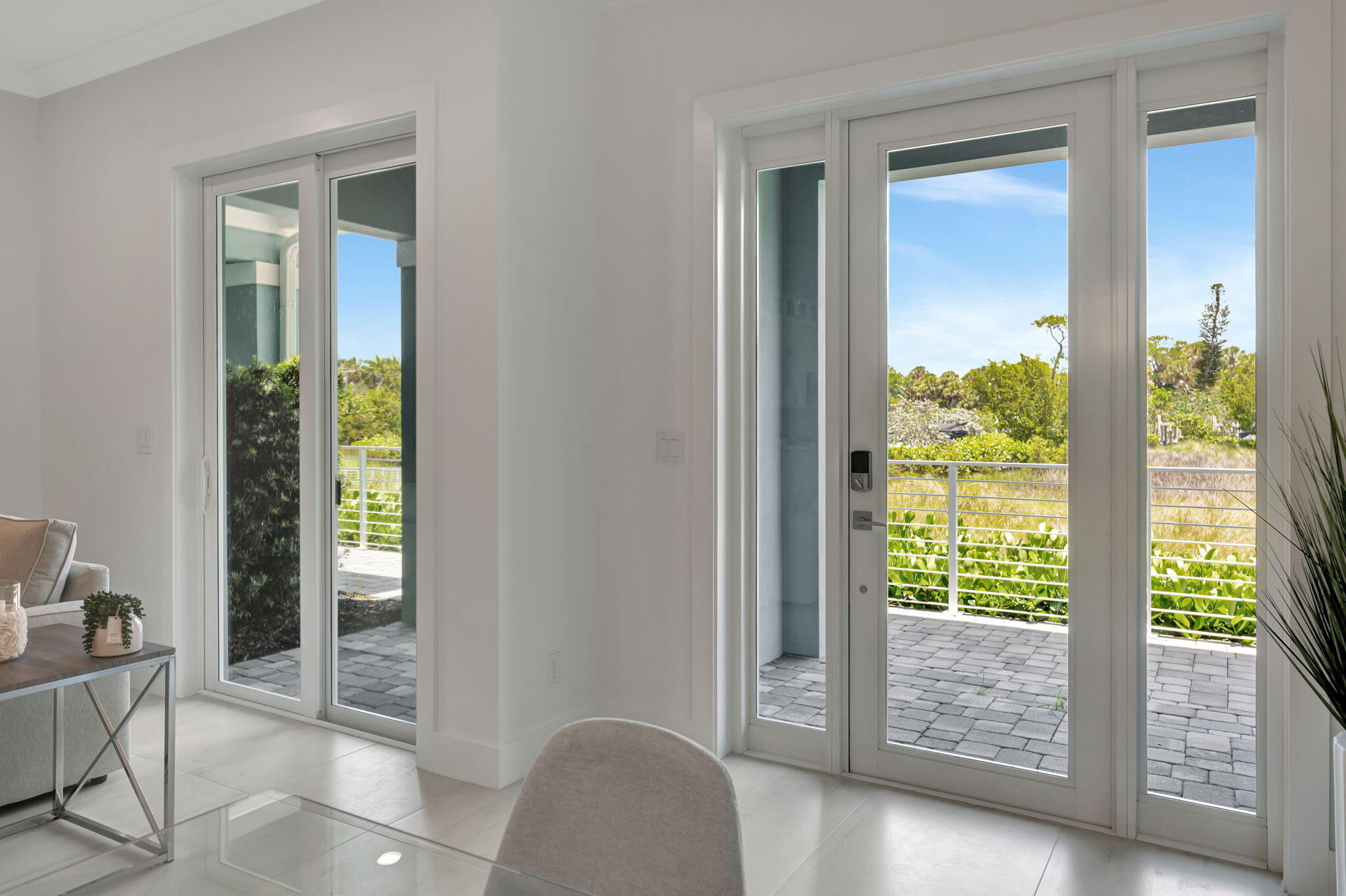 Living area with wide glass doors opening onto a paved patio and greenery.