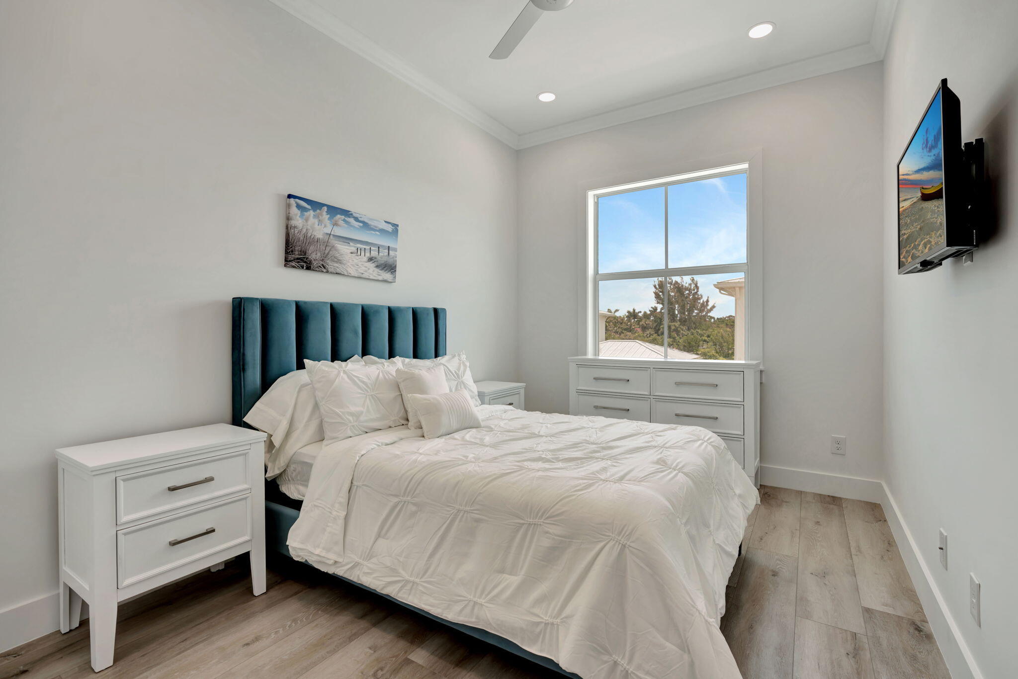 Bedroom with a white bed, teal headboard, and a window overlooking greenery.