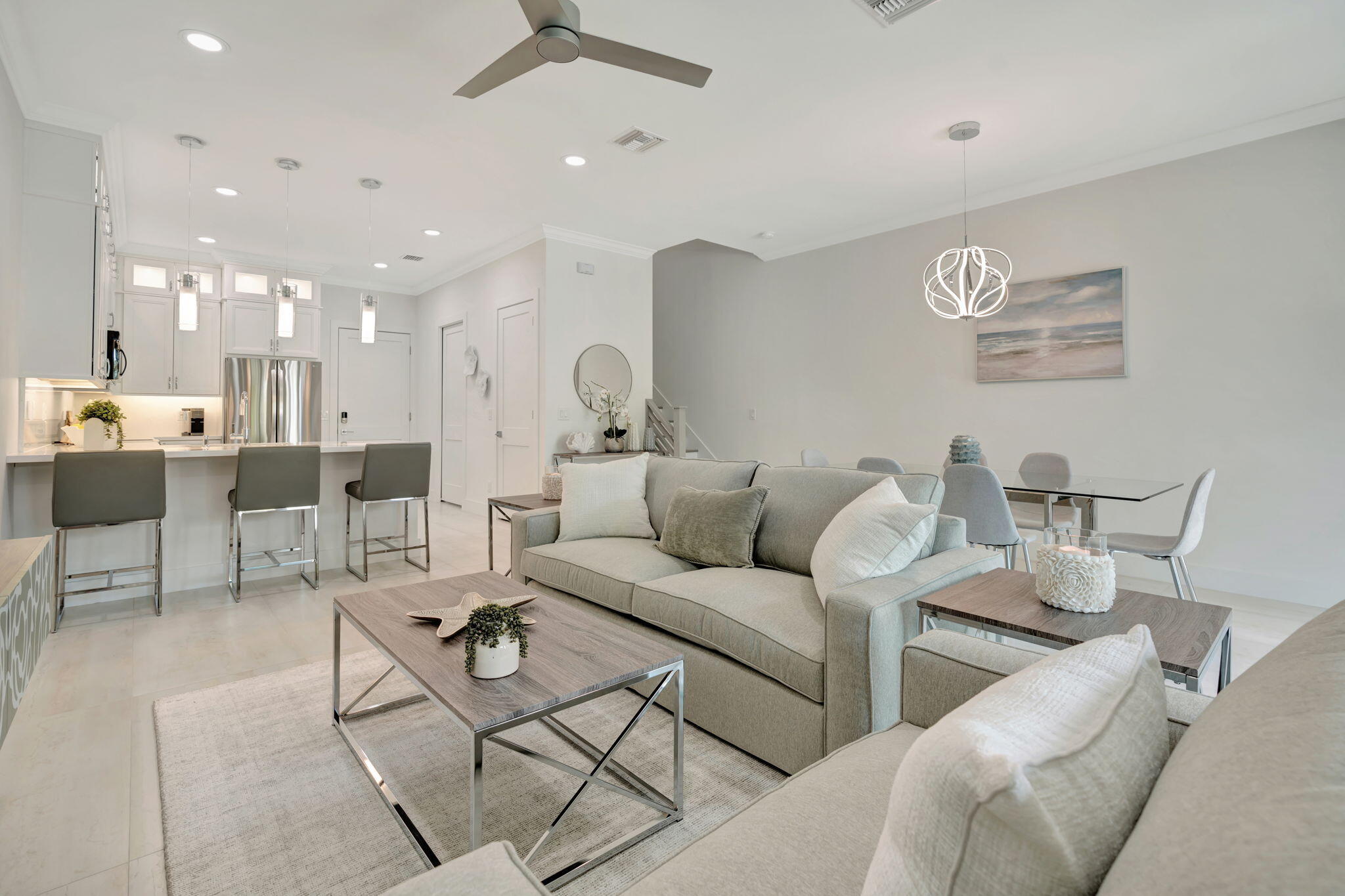Open-plan living room with gray sectional, dining table, and bright white kitchen.