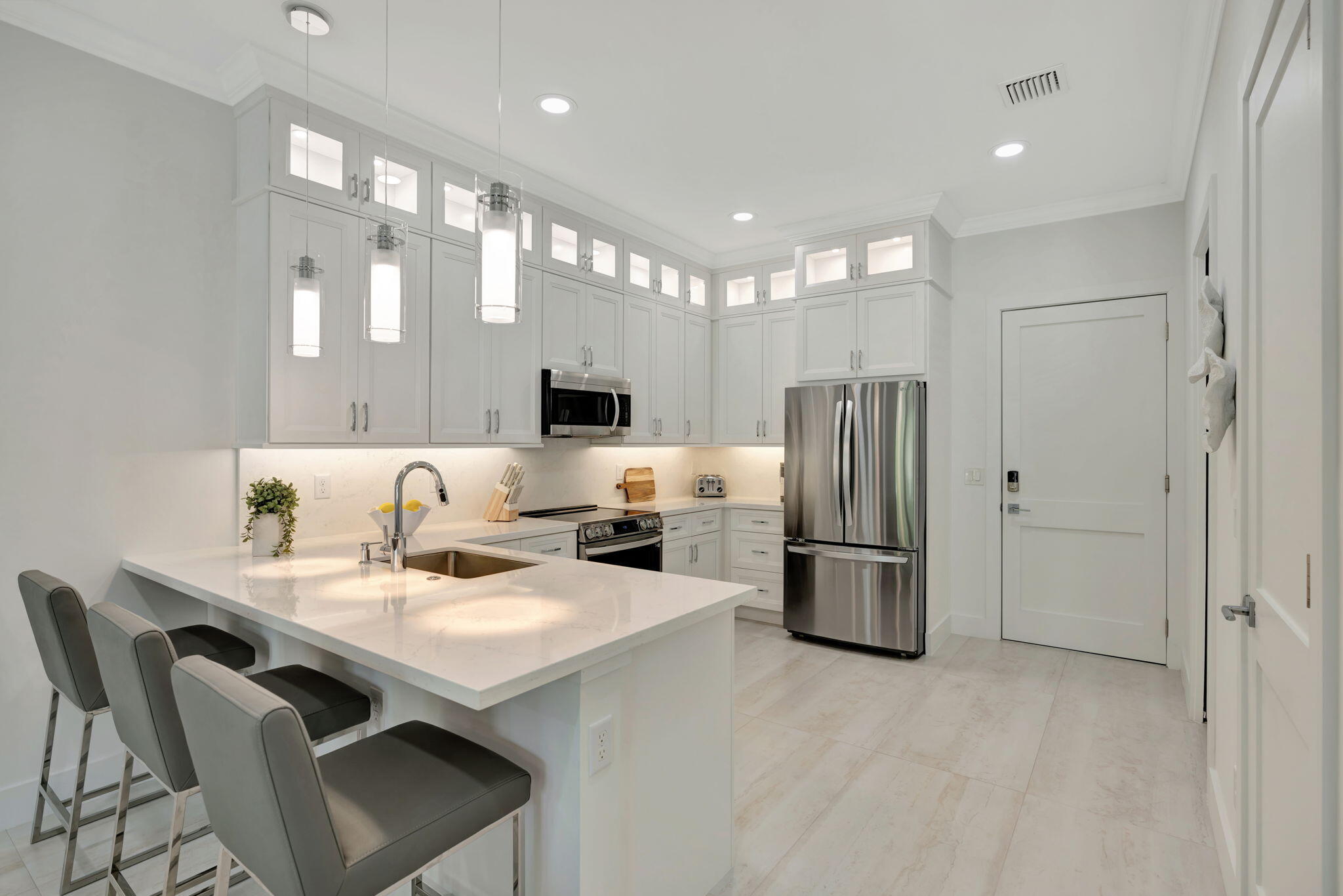 Kitchen with a large white island, gray bar stools, ceiling-height cabinets, and stainless steel appliances.