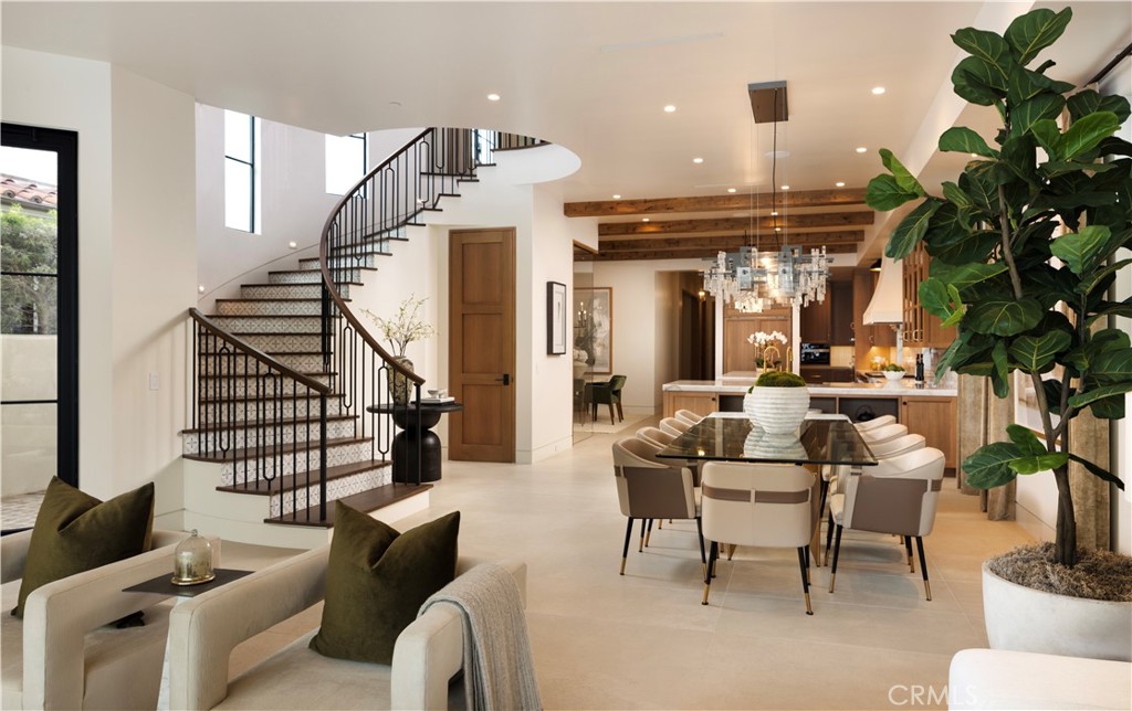 Open-plan living and dining area with a curved staircase, exposed beams, and a kitchen beyond.