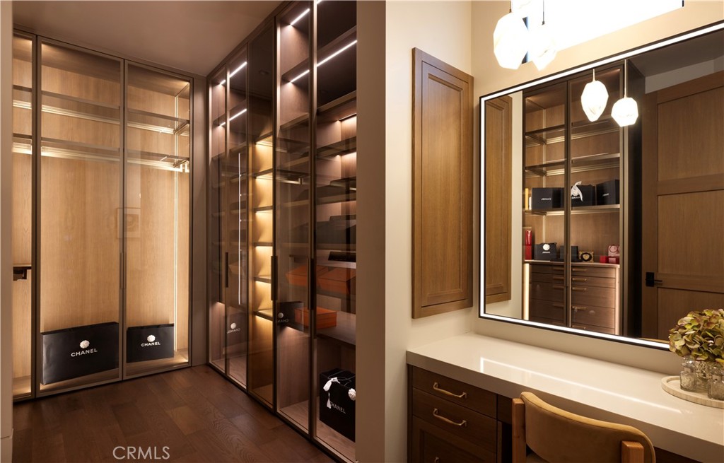 Walk-in closet with illuminated glass-fronted cabinets and an adjoining vanity with a large mirror.