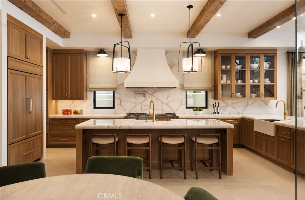 Kitchen with a large marble island, dark wood cabinetry, and exposed ceiling beams.