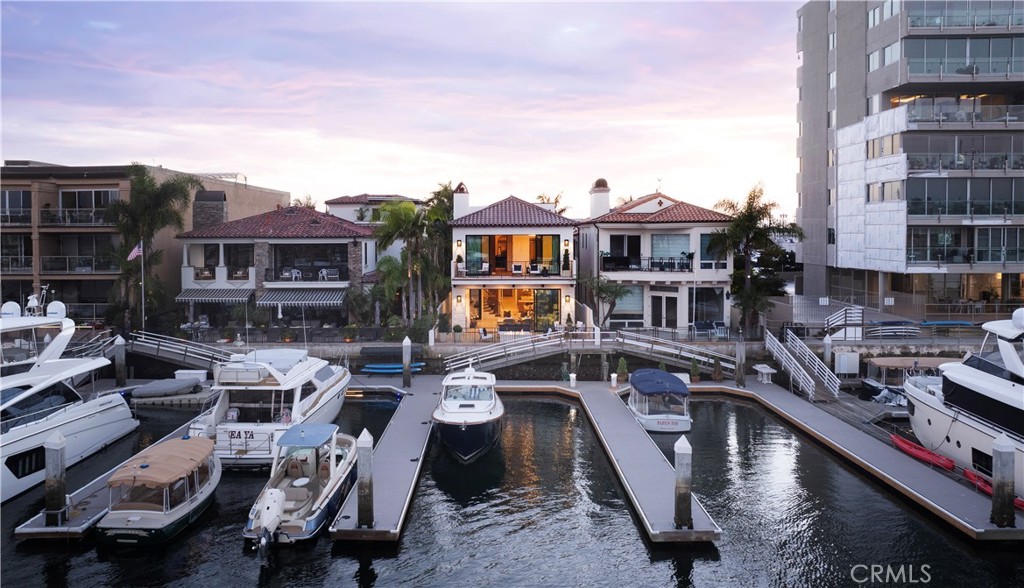Waterfront home at dusk with a private dock, boats, and neighboring marina buildings.