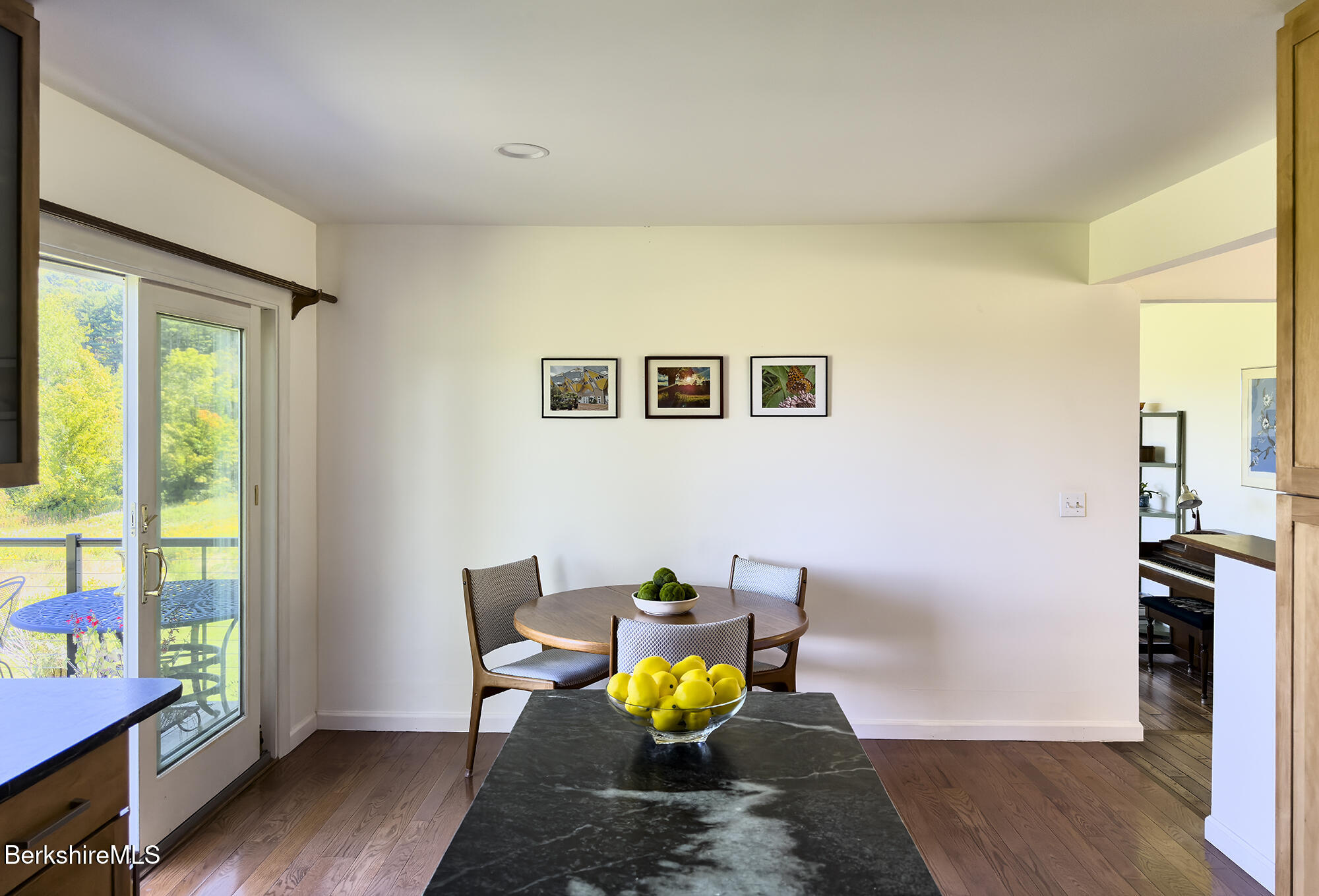 Dining area with a round wooden table beside a sliding glass door opening to a tree-lined view.