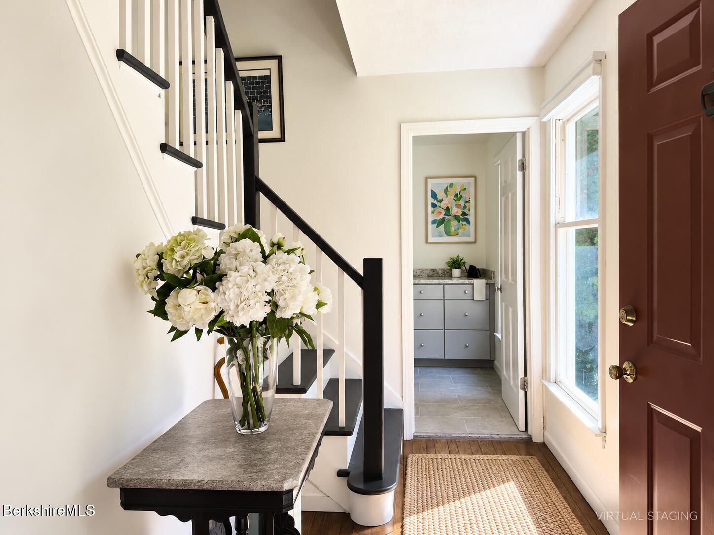 Entry foyer with a red front door, black-and-white staircase, and flower-topped console table.