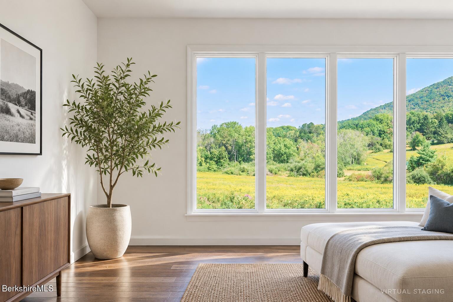 Virtually staged living room with broad windows overlooking a sunny meadow and wooded hills.