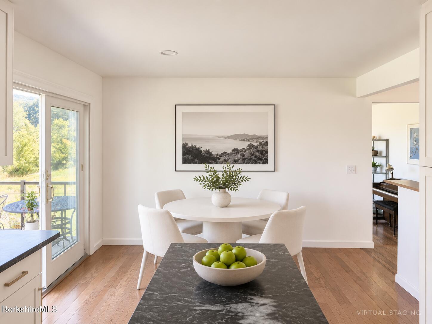 Bright dining area with a round white table, hardwood floors, and glass doors opening to greenery.