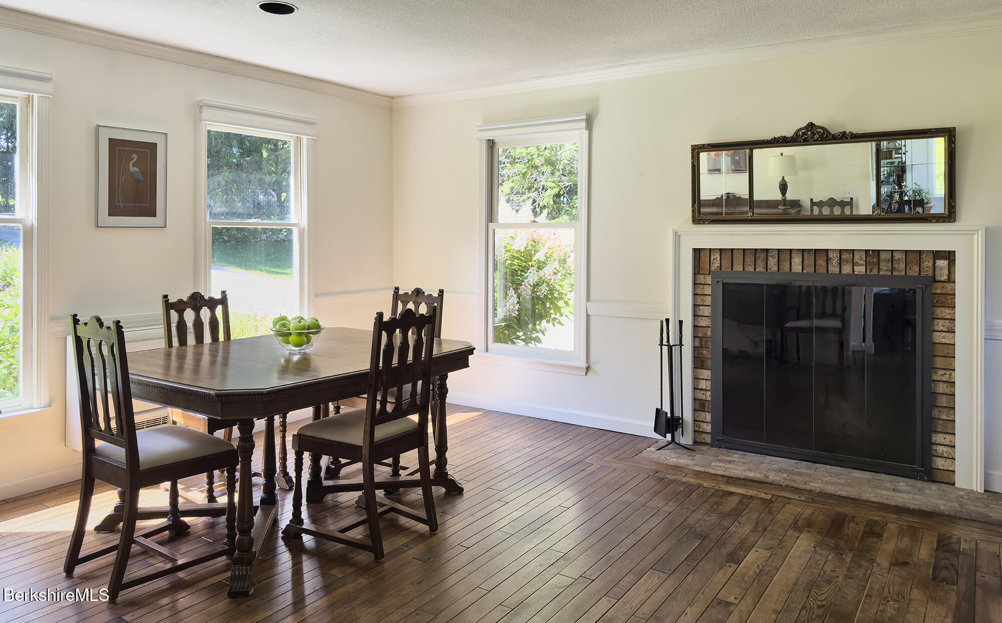 Dining room with a brick fireplace, dark wood table, and sunlit windows.